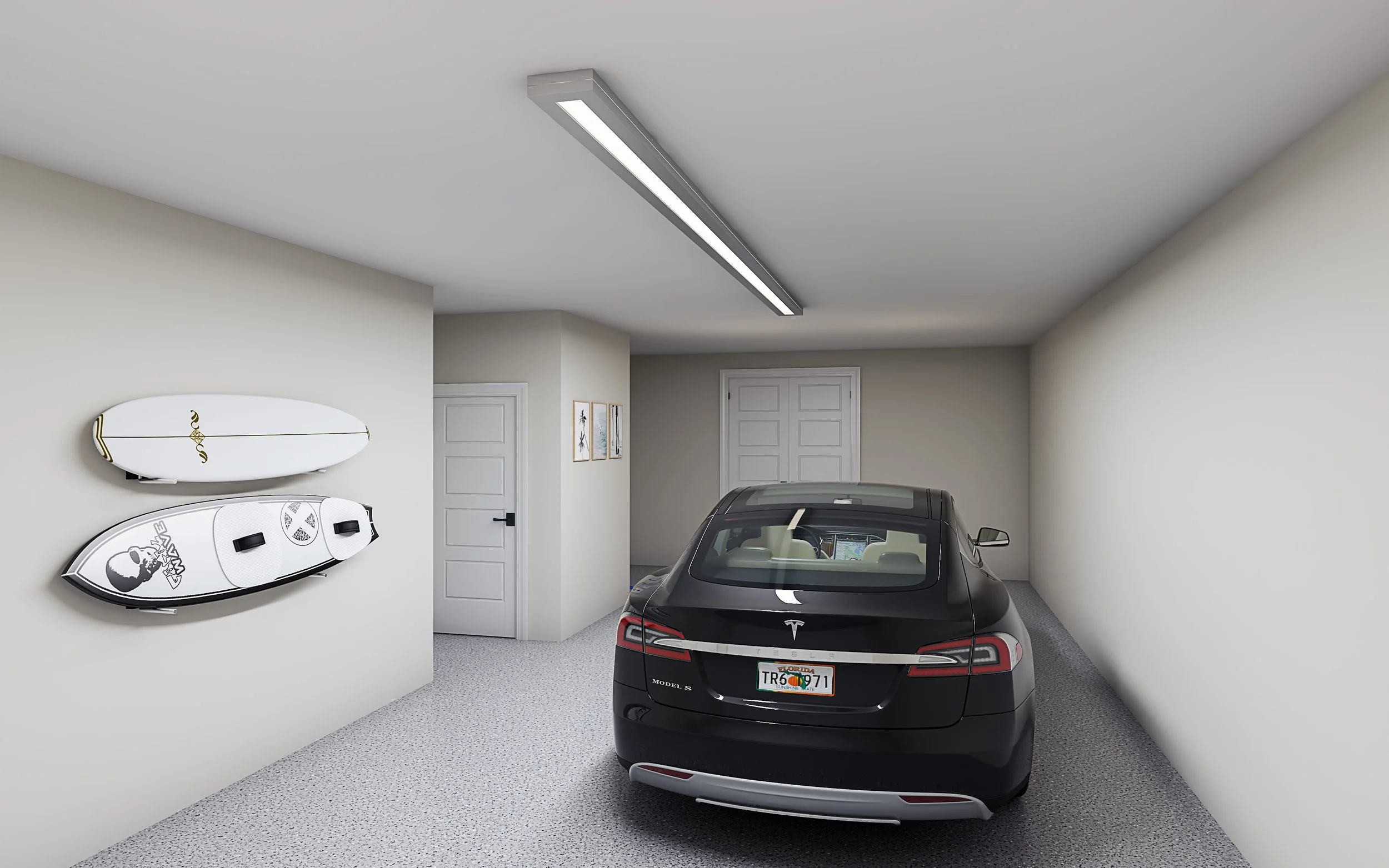 A black Tesla Model S in a clean, organized garage with white walls. Two surfboards are mounted on the left wall, and three framed pictures are hanging on the wall near the back door. The garage has a gray speckled floor and a fluorescent ceiling lig