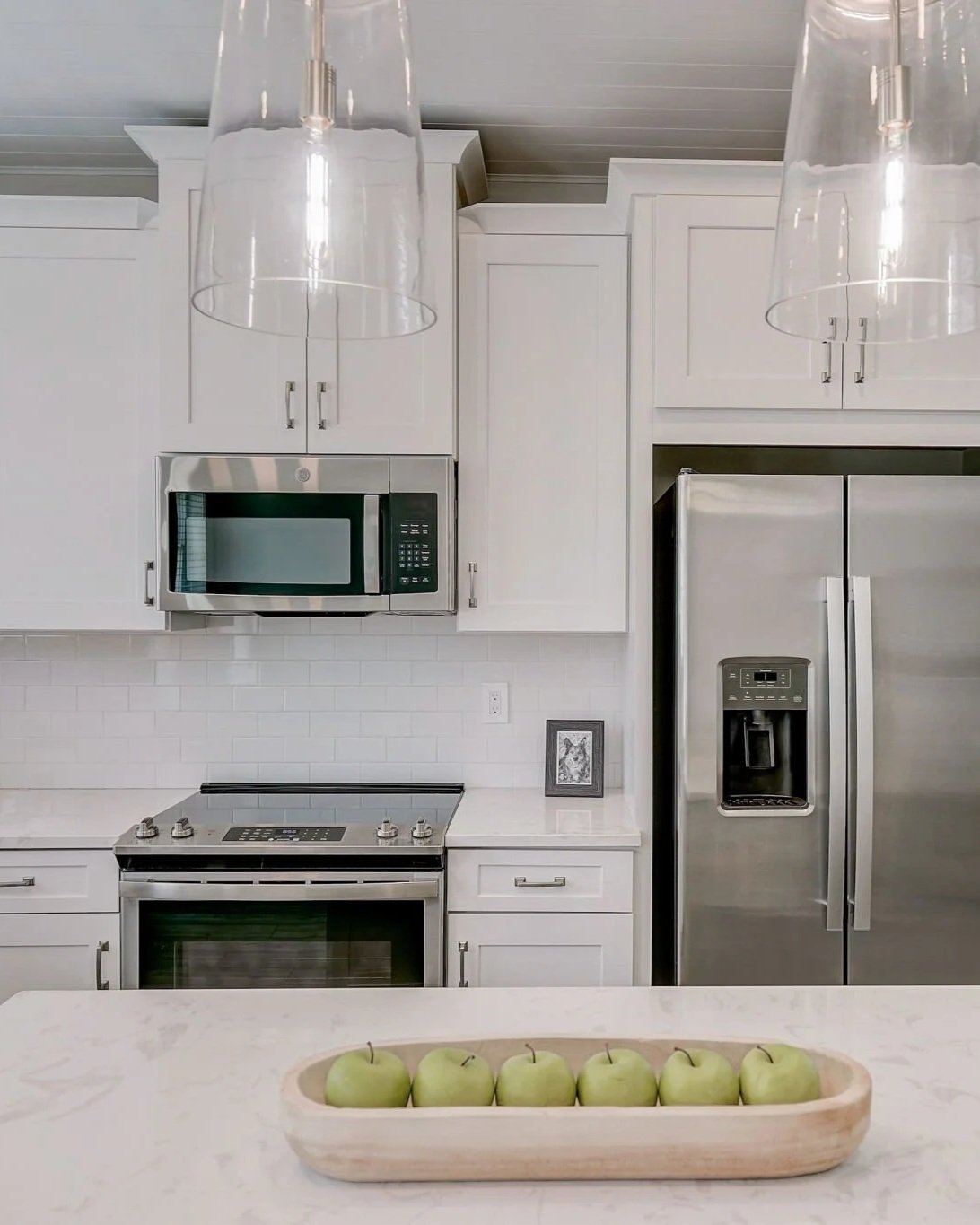 Modern kitchen with white cabinets, stainless steel appliances, and a decorative tray with green apples on the counter.