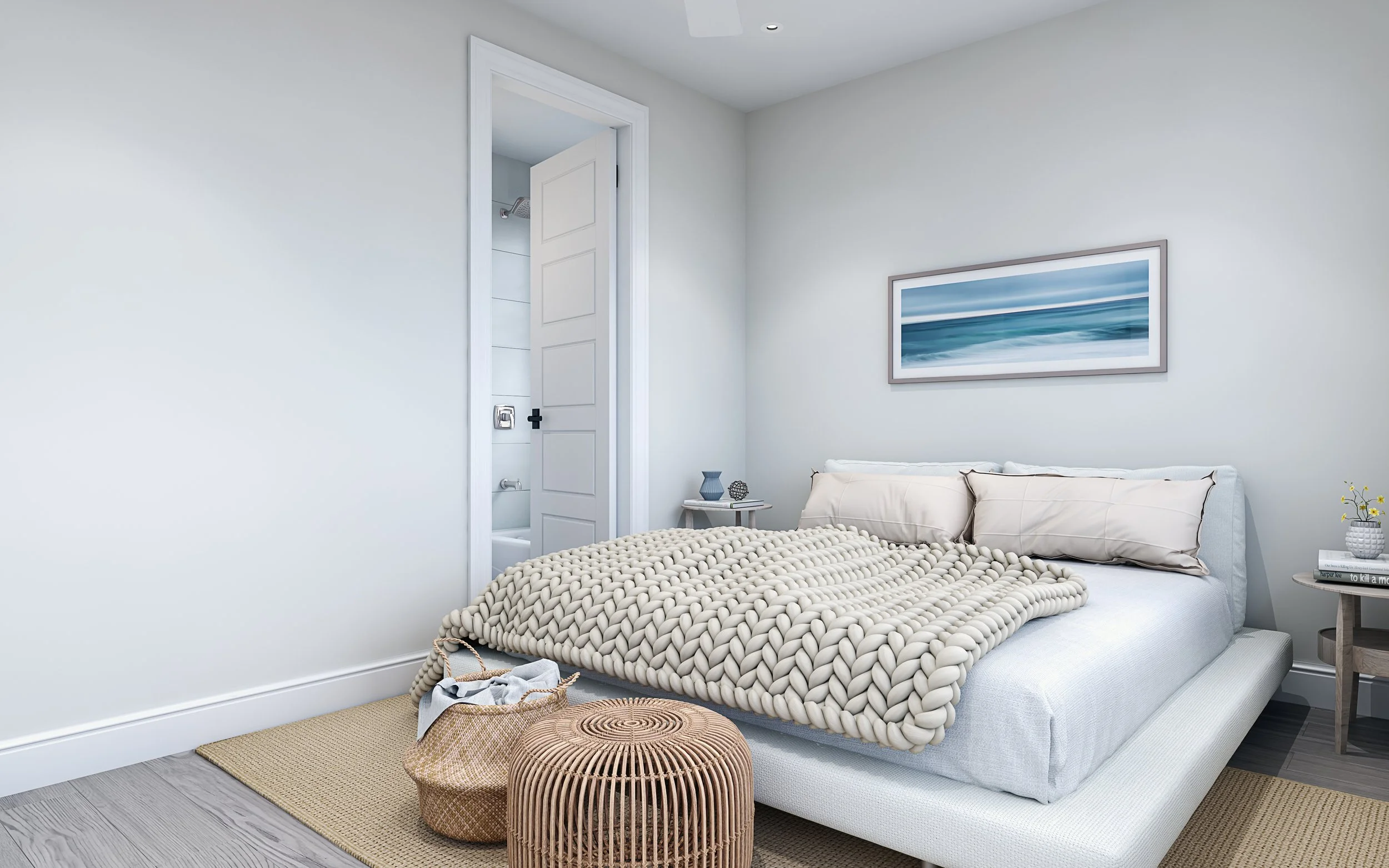 Minimalist bedroom with a white bed featuring thick knitted blanket and beige pillows, a small side table with decorative items, a woven basket, a cylindrical stool, and artwork of the ocean on the wall.