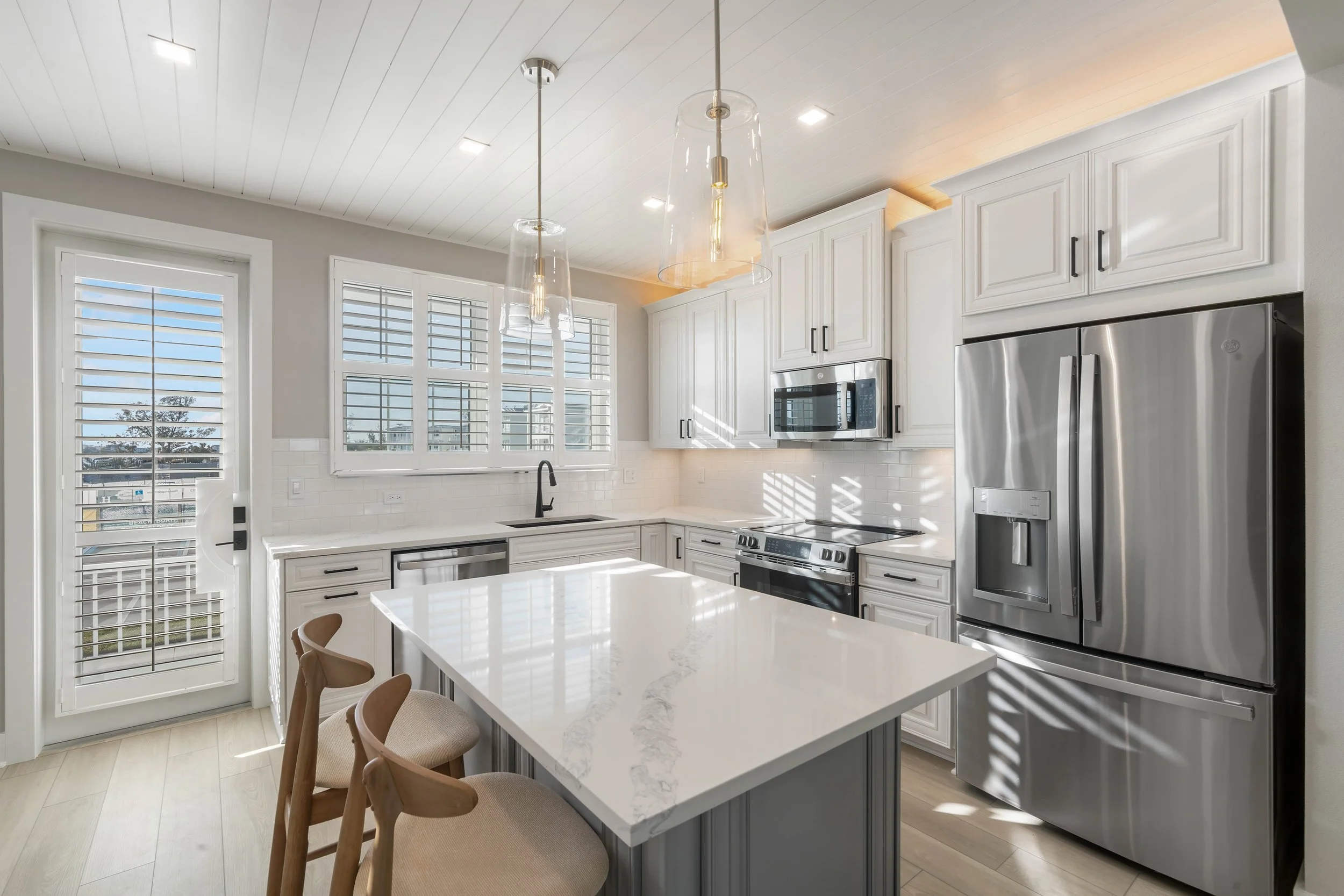 Modern kitchen with white cabinets, stainless steel appliances, a marble island, and pendant lighting.