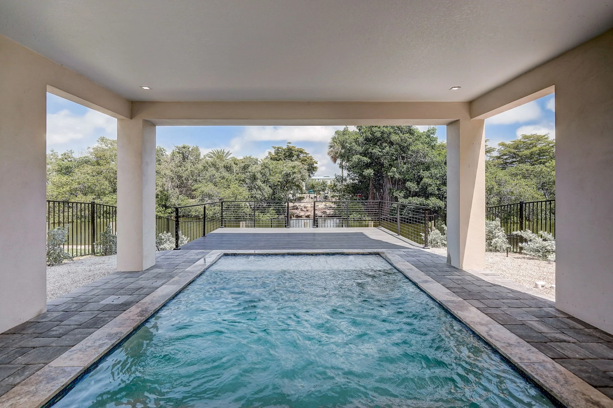 Covered outdoor pool with a view of green trees and a canal in the distance.