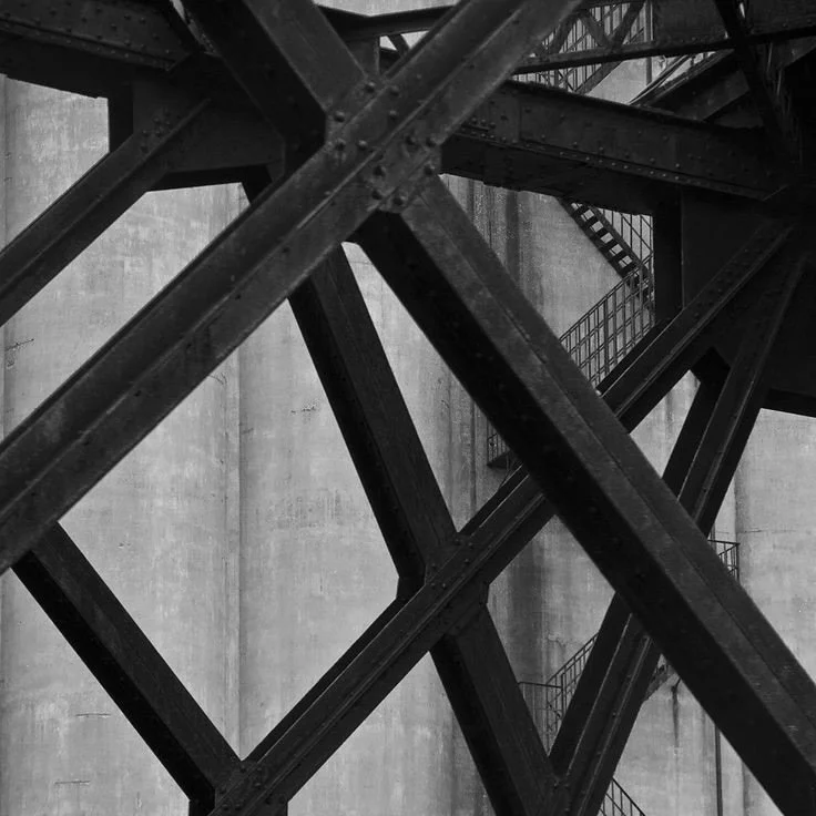 Black metal industrial staircase and structural support beams against concrete wall, with visible safety stairs.
