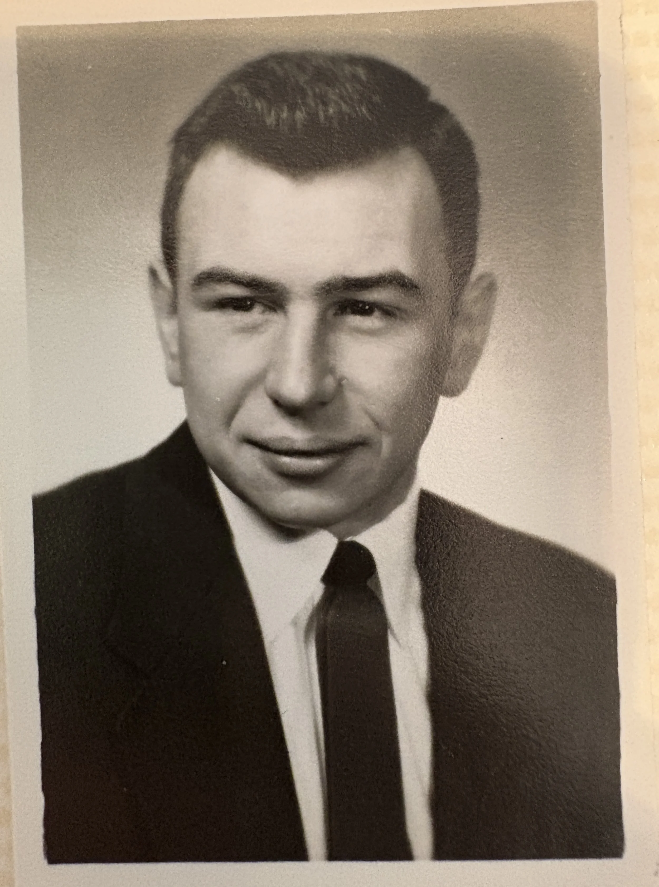 Black-and-white portrait of a young man in a suit and tie, with short, neatly combed hair.