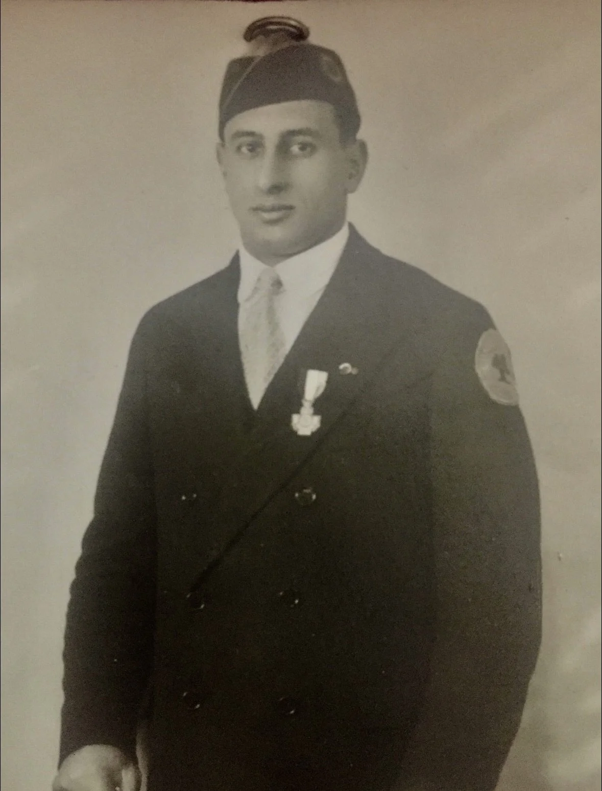 Black and white photograph of a man in a military or police uniform with medals, wearing a peaked cap and standing against a plain background.