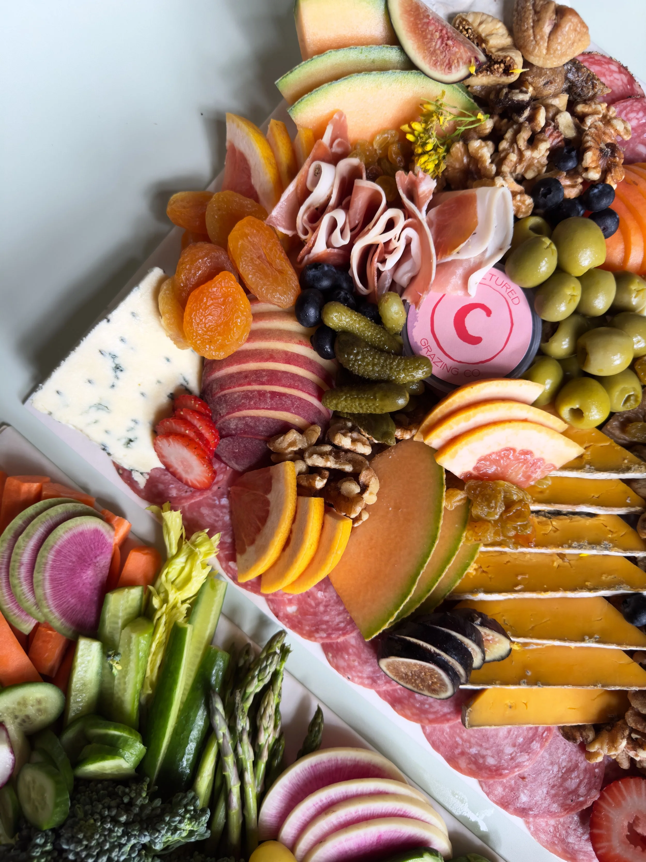 Close-up of a cheese and charcuterie board with grapes, sliced melons, strawberries, figs, nuts, cured meats, cheese, and fresh vegetables.