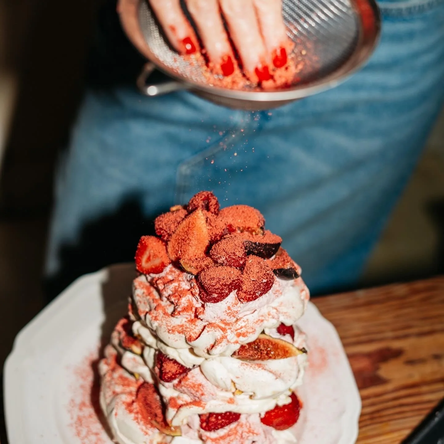 A person sprinkles ground red powder over a dessert topped with strawberries and whipped cream.