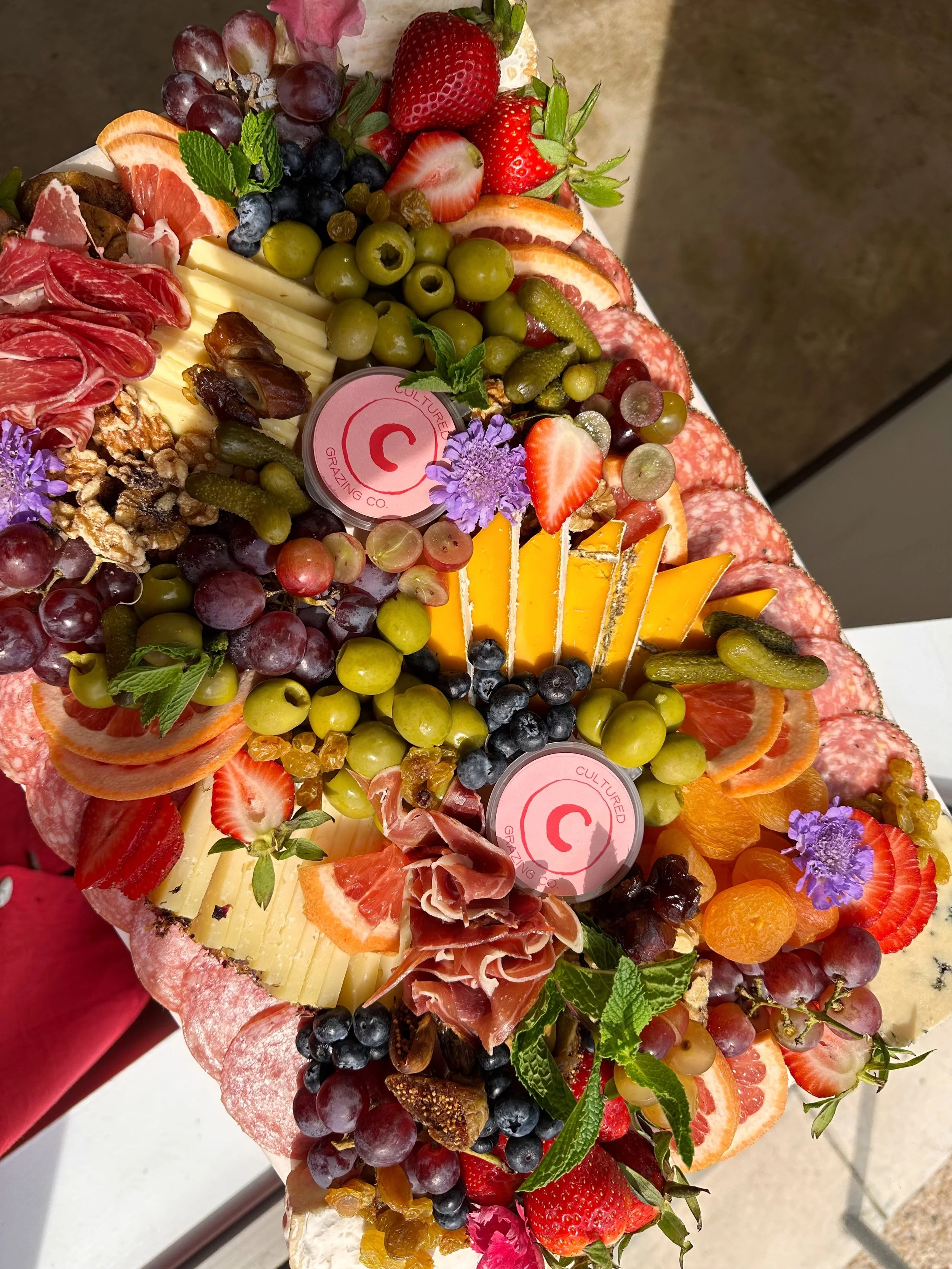 A colorful charcuterie board with an assortment of fresh fruits, cheese, cured meats, nuts, and herbs.