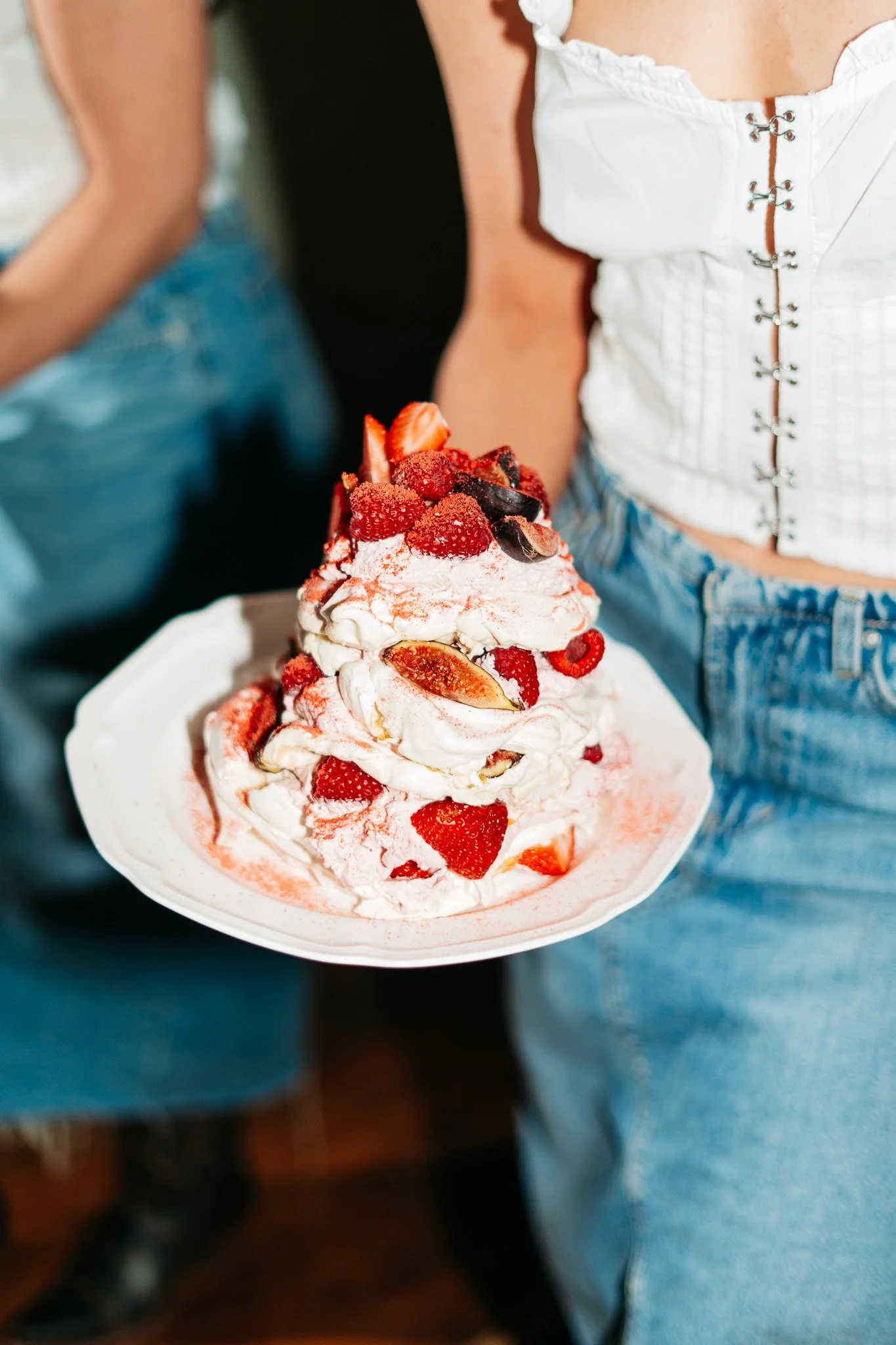 A person holding a plate with a large serving of whipped cream topped with strawberries, raspberries, and other berries.
