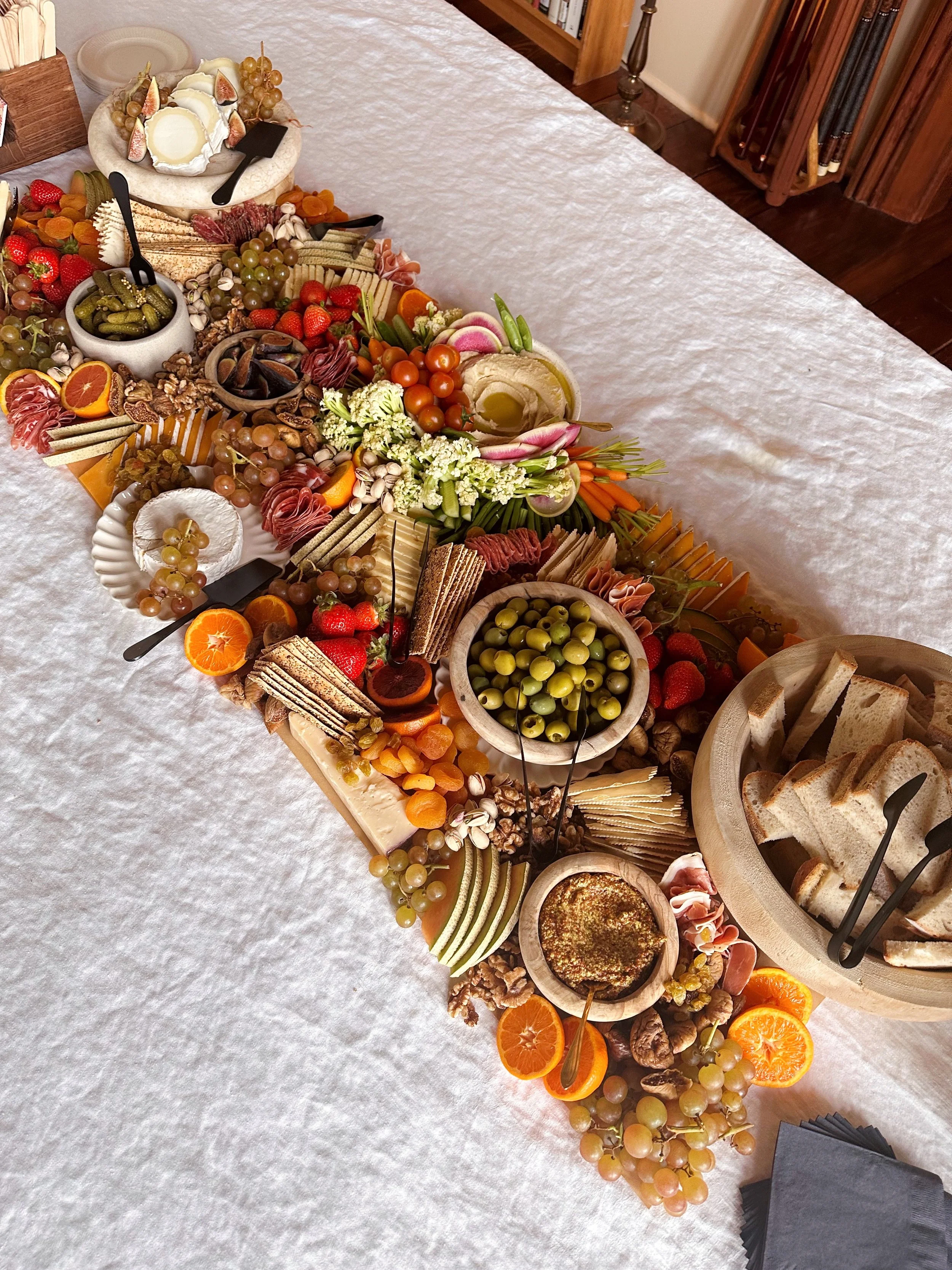 A charcuterie board with various cheeses, fruits, nuts, crackers, and vegetables on a white tablecloth.