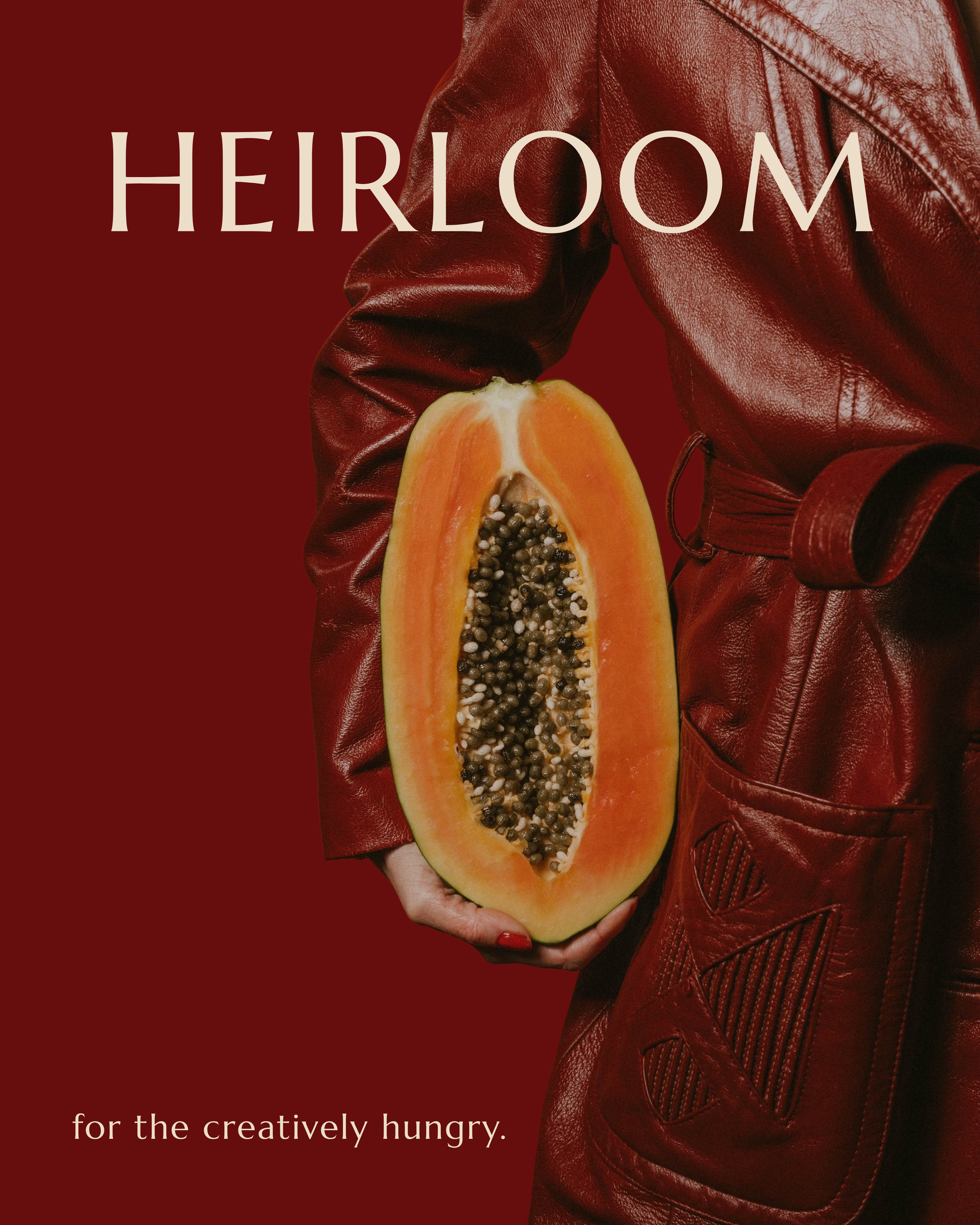 Person in a red leather jacket holding a halved papaya with black seeds on a matching red background. The text reads 'HEIRLOOM' at the top and 'for the creatively hungry.' at the bottom.