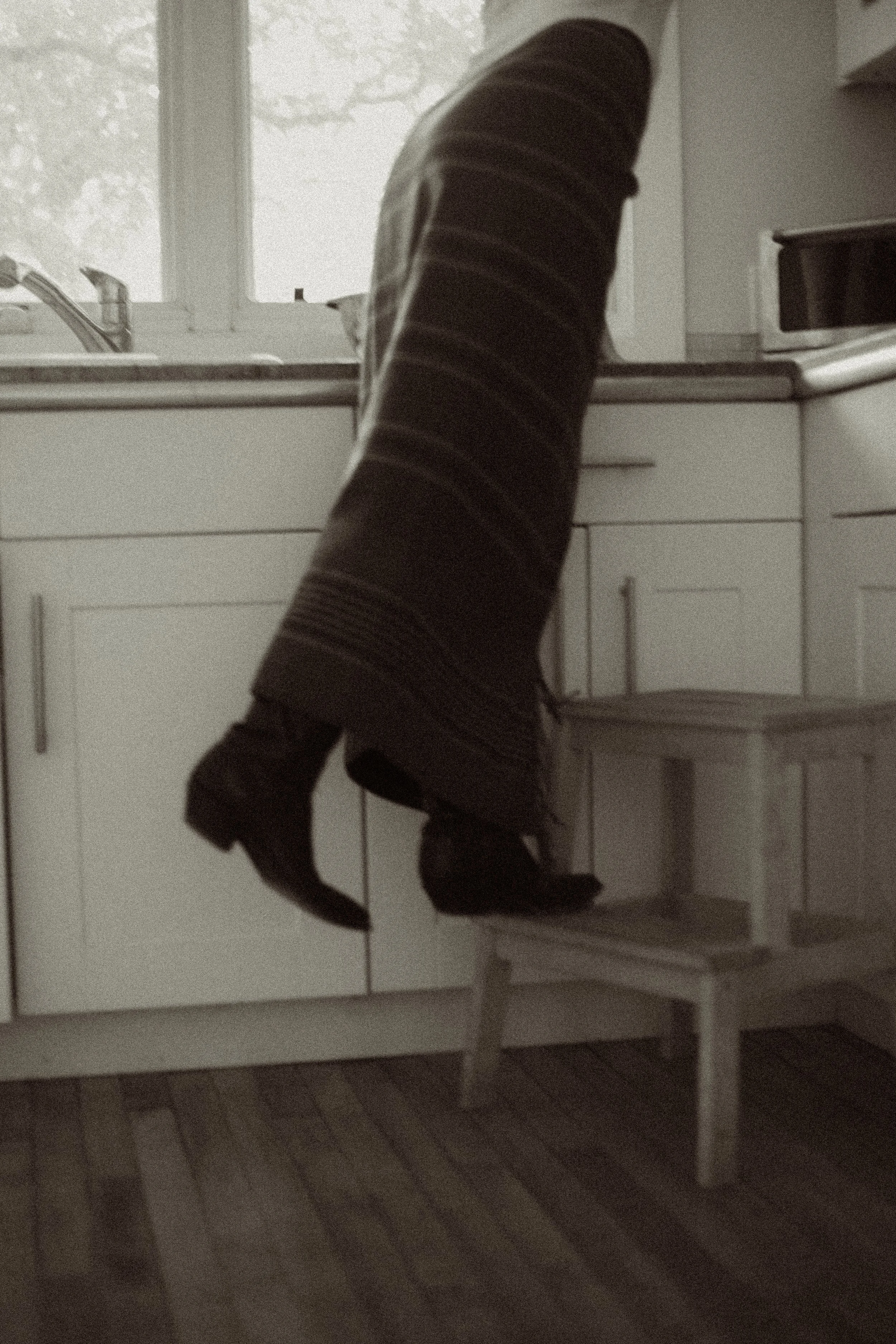 Person with a long striped coat and high-heeled boots climbing onto a kitchen counter through a step stool.
