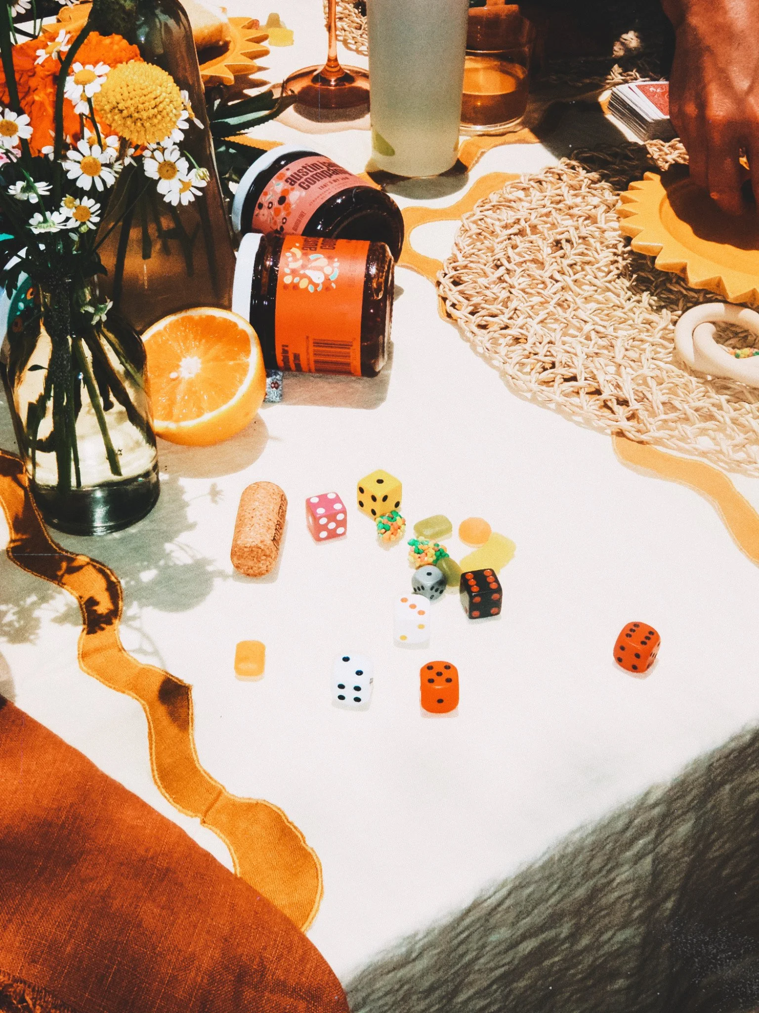 A table with a floral centerpiece, two bottles of medication, a half orange, and various scattered dice and candy.