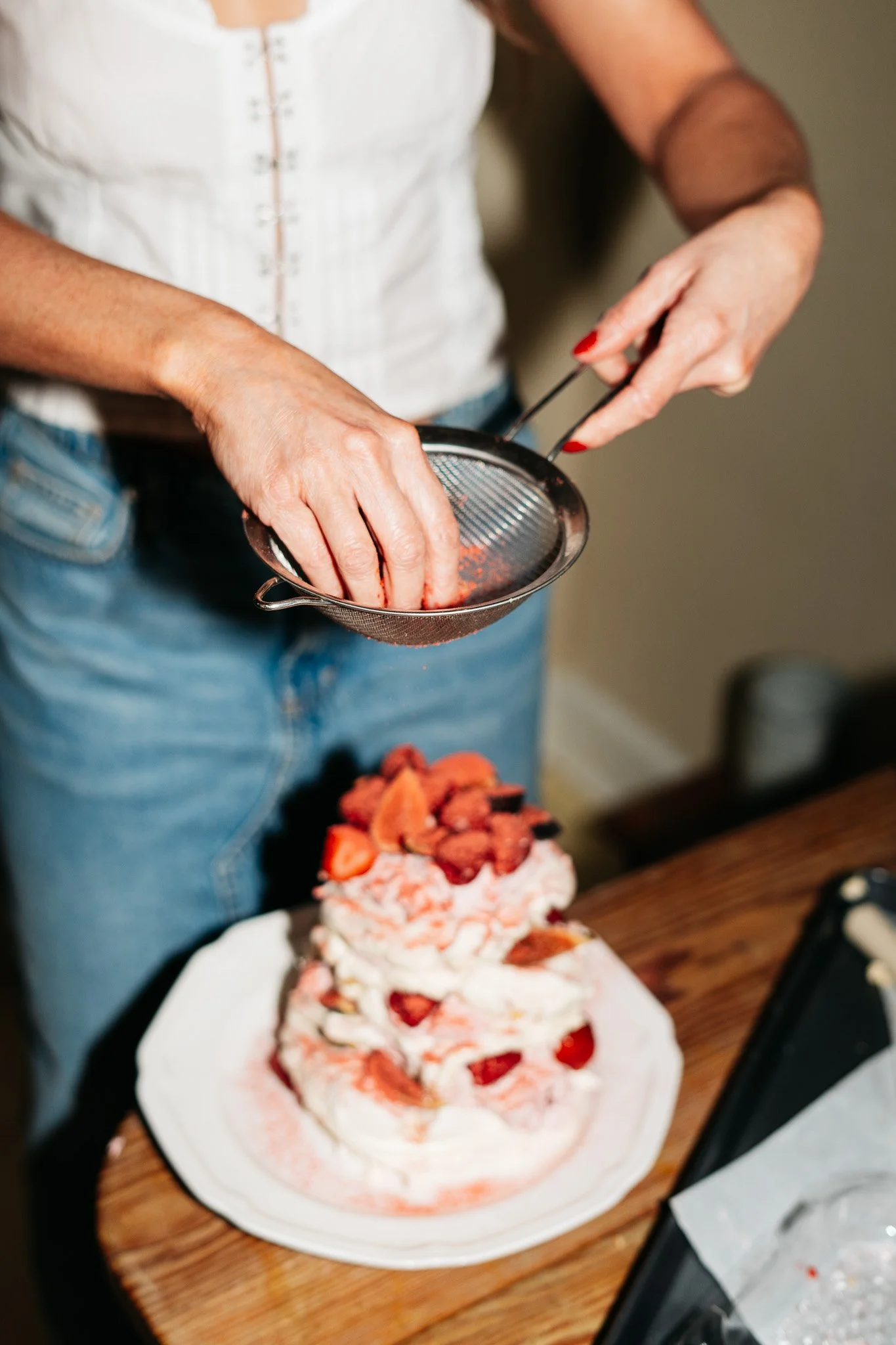 Person sprinkling powdered topping on a layered strawberry shortcake dessert