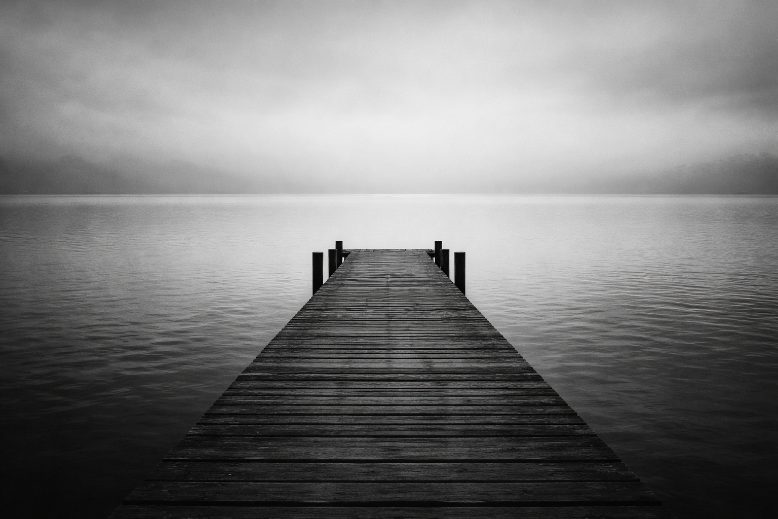 Wooden pier extending into calm water under an overcast sky, symbolizing openness and a path forward.