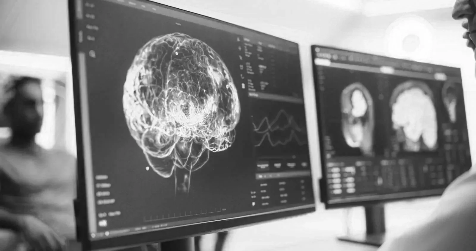 Black and white photo of a scientist analyzing brain scans on large computer screens in a laboratory setting.