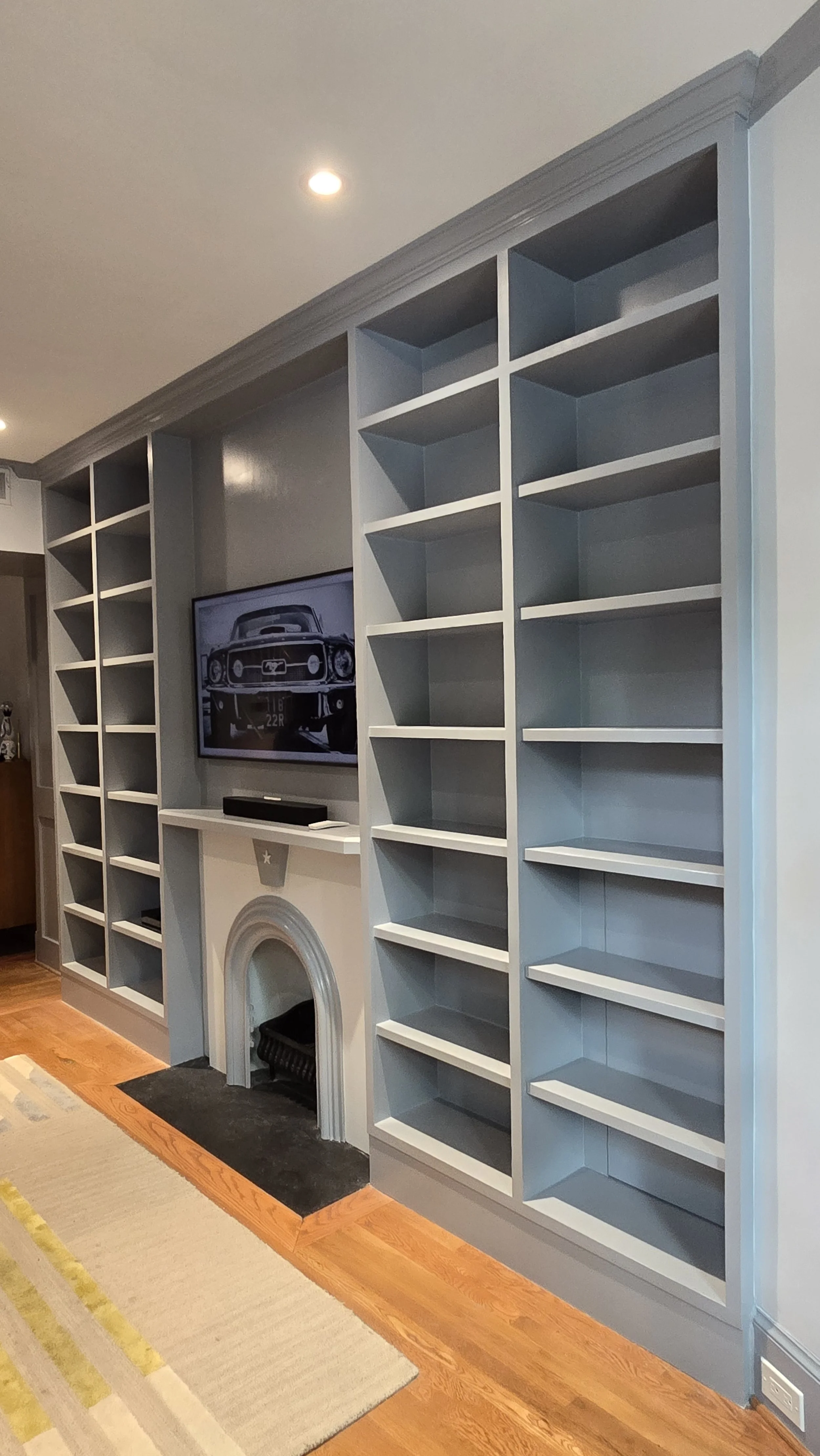 Living room with built-in blue shelves, a television above a white fireplace, and hardwood floors.