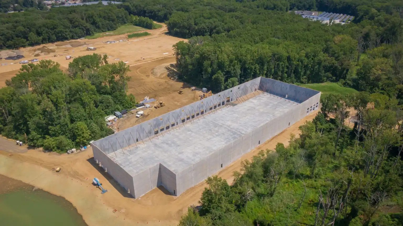 Aerial view of a large construction site where a building is being erected, surrounded by trees and some vehicles.