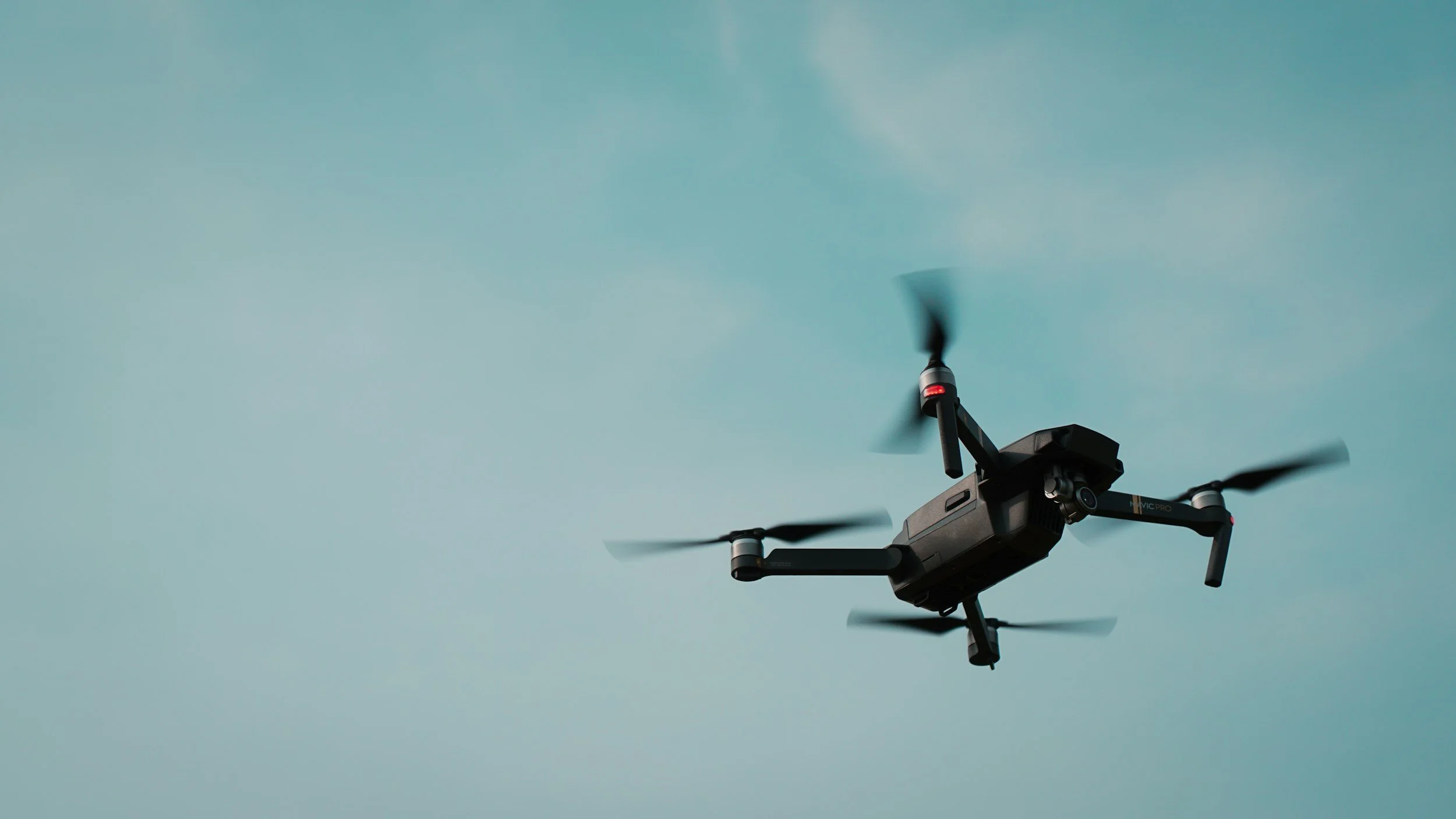 A black drone with four propellers flying against a light blue sky.