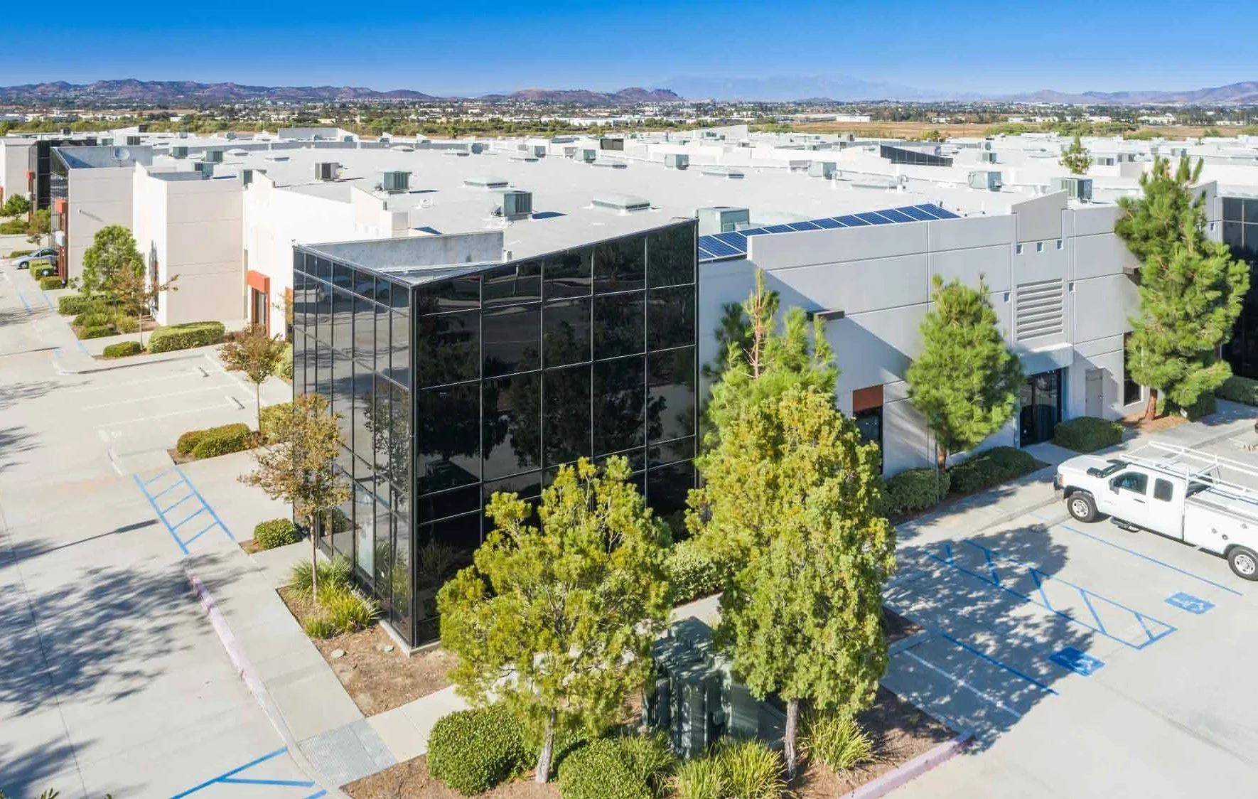 Aerial drone image of a commercial office and warehouse complex with parking lots, trees, and industrial rooftops. Commercial property marketing and inspection photography for businesses.