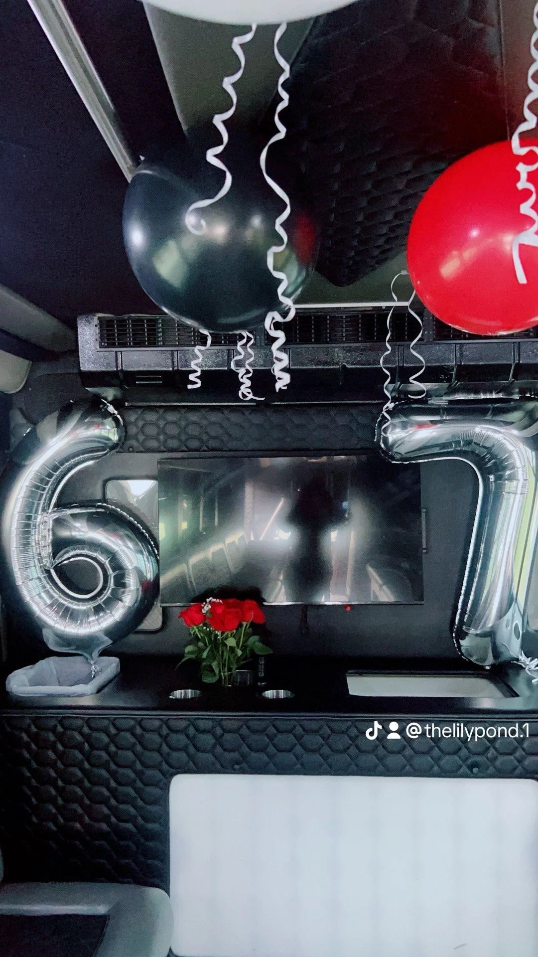 Celebration decorations inside a vehicle, including black and red balloons, white ribbon streamers, a small vase of red roses, and a silver number "6" balloon.