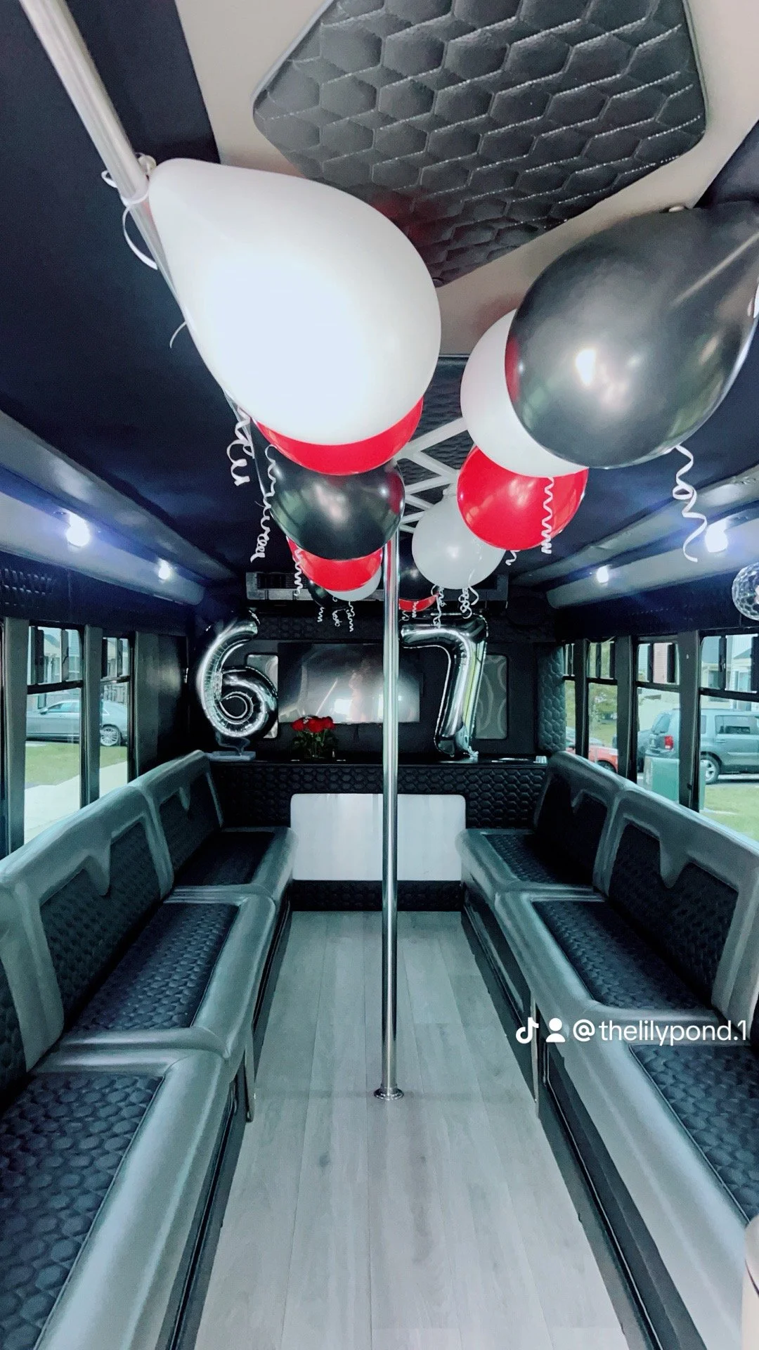 Interior of a bus decorated for a celebration with black, white, and red balloons hanging from the ceiling, large silver '60' and '70' balloons, a rose bouquet on the back counter, and windows on both sides.