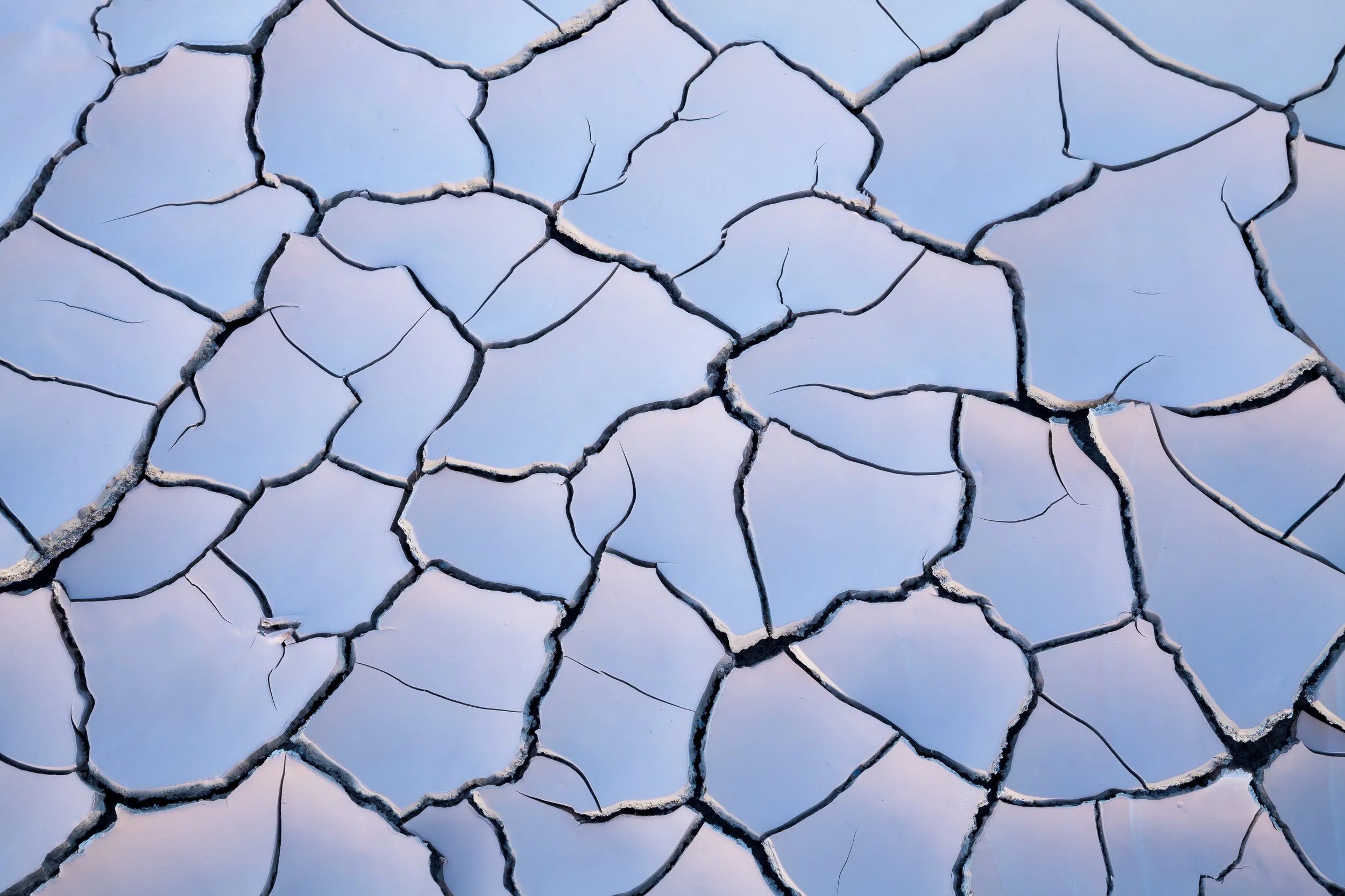 Close-up of cracked dry earth with a blue sky in the background by Sarah Marino.
