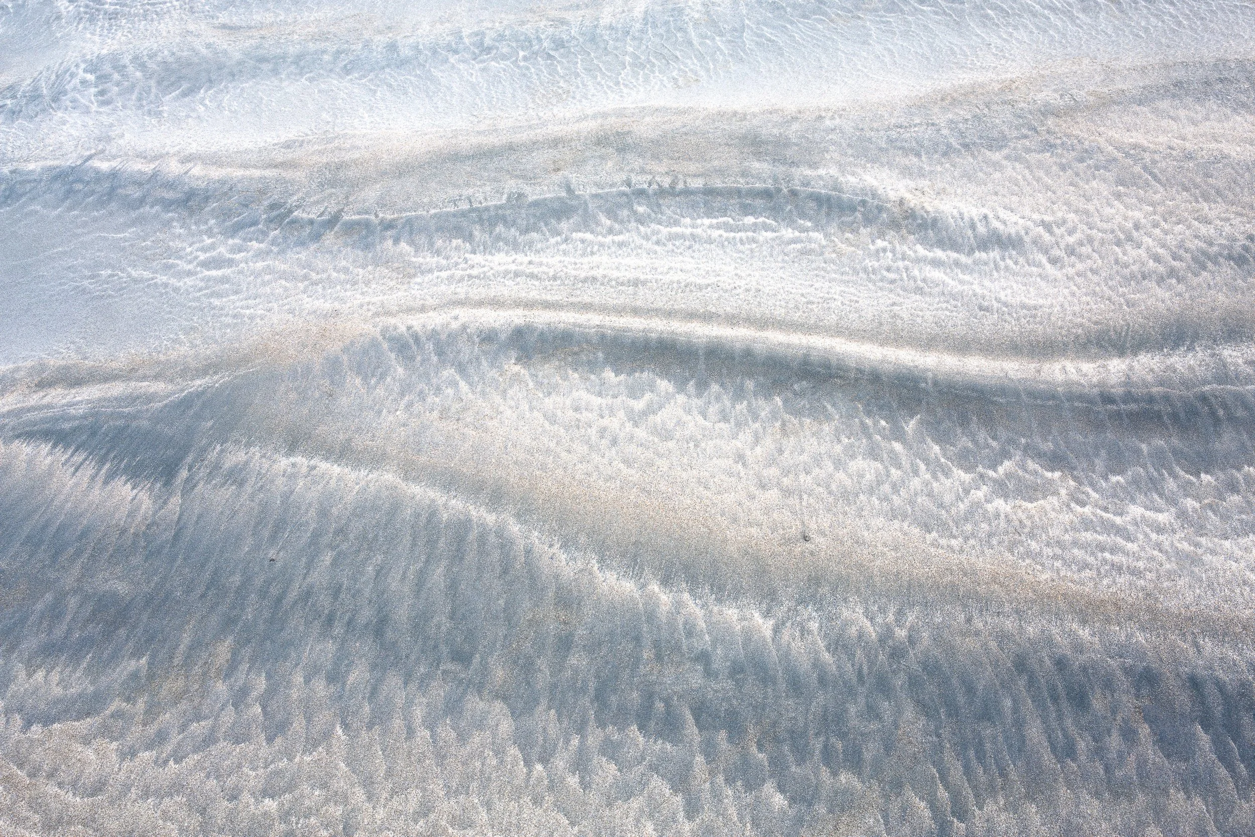 Close-up of sand with textured, wavy patterns and subtle shadows by Anna Morgan.