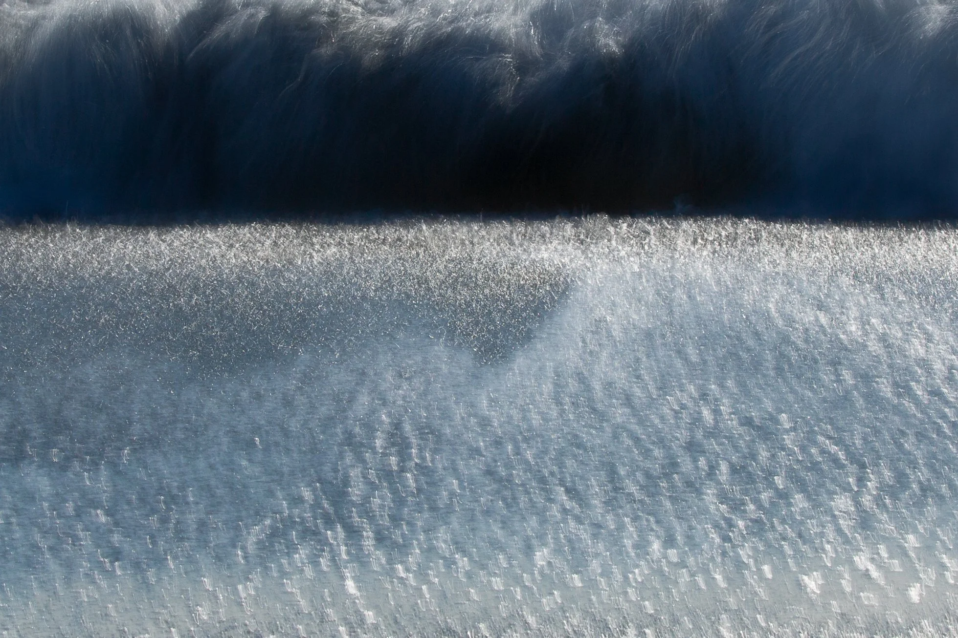 Close-up of a wave crashing onto flat surface, with sunlight reflecting off the sand by Anna Morgan.