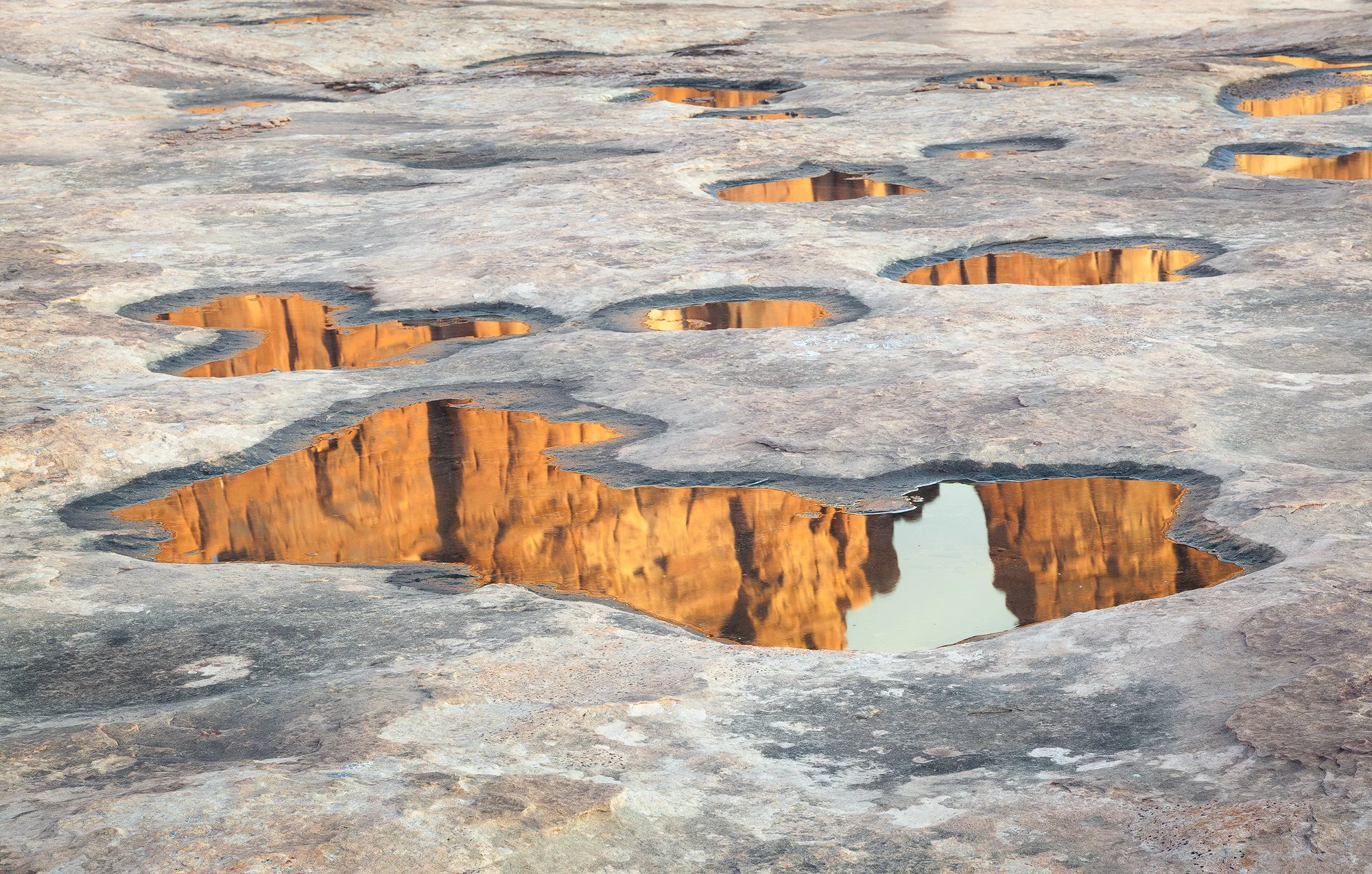 Rocky terrain with small pools of water reflecting orange-hued cliffs at sunset by Charlotte Gibb.