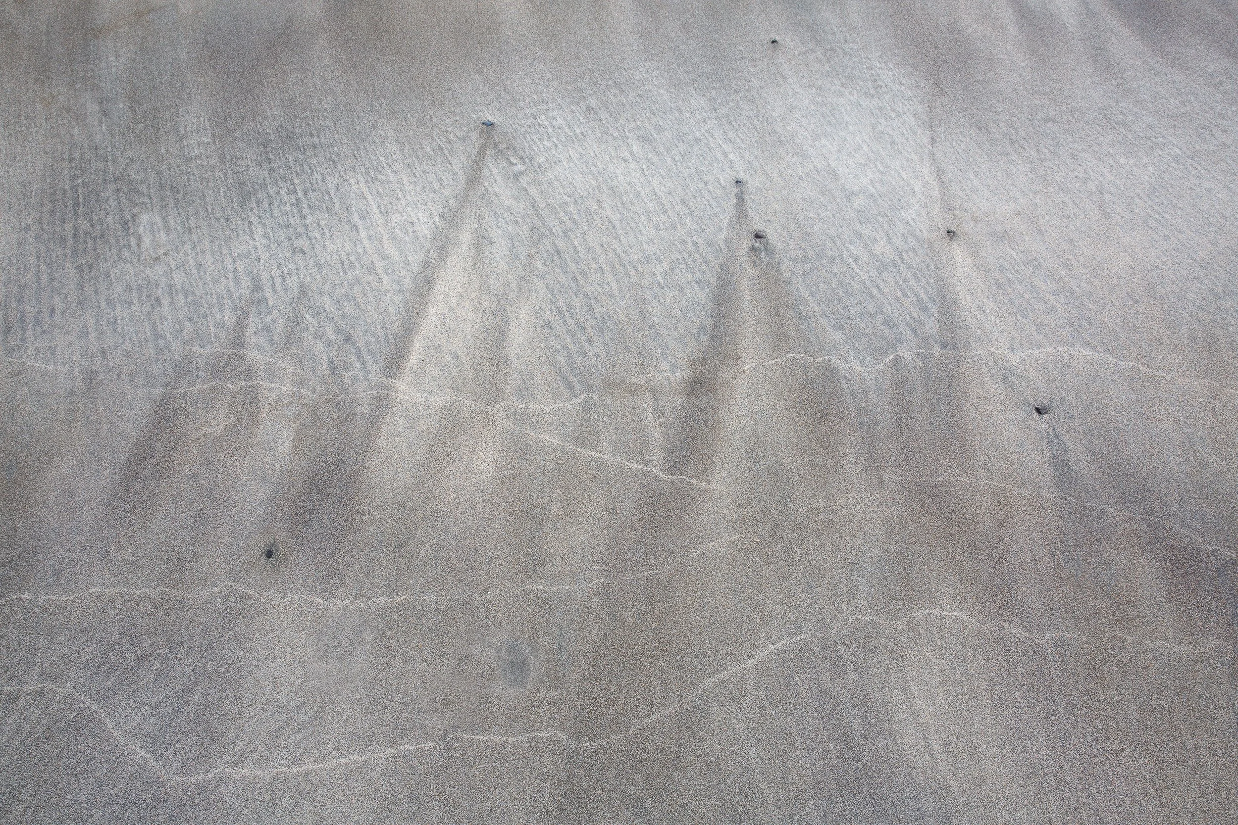 Close-up of sand with faint lines and small holes by Anna Morgan.