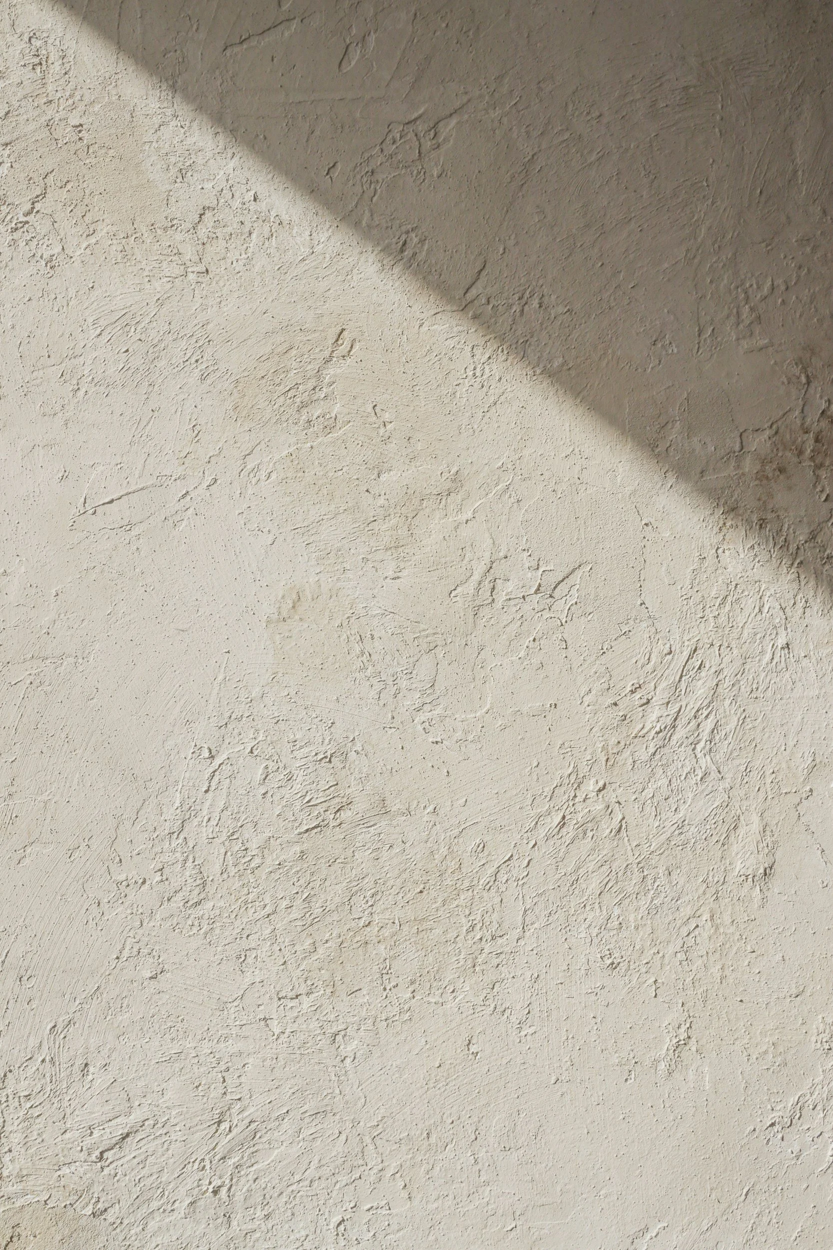 Close-up view of a textured beige wall with a diagonal shadow cast across it.
