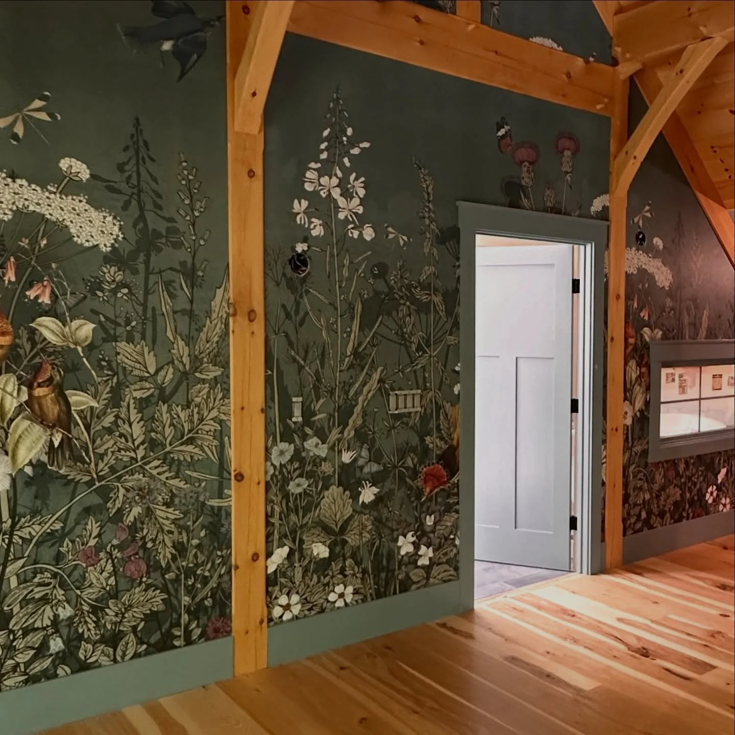 Interior view of a room with floral wallpaper, wooden framing, and a doorway leading to another room or hallway.