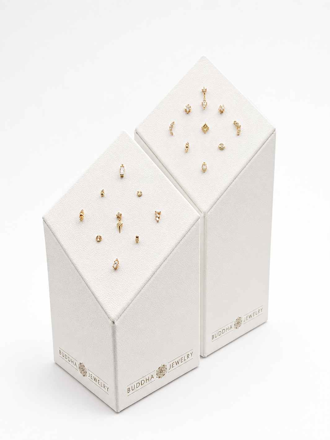 Deux boîtes blanches contenant des boucles d'oreilles en or avec des détails variés, étiquetées 'Buddha Jewelry'.