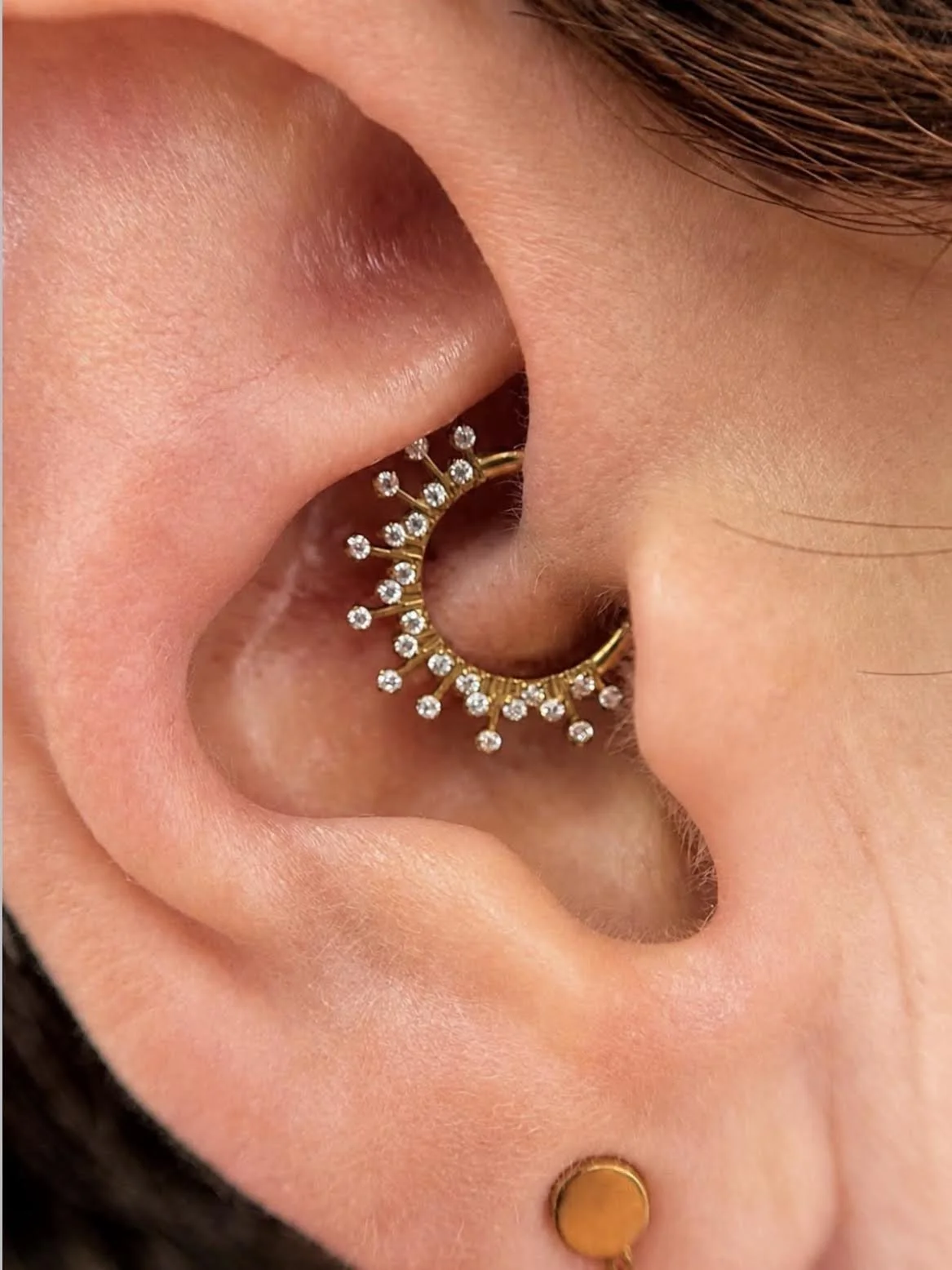 Zoom sur une oreille portant plusieurs piercings : une boucle d'oreille en or ornée de diamants, un petit piercing en or avec un disque en or.
