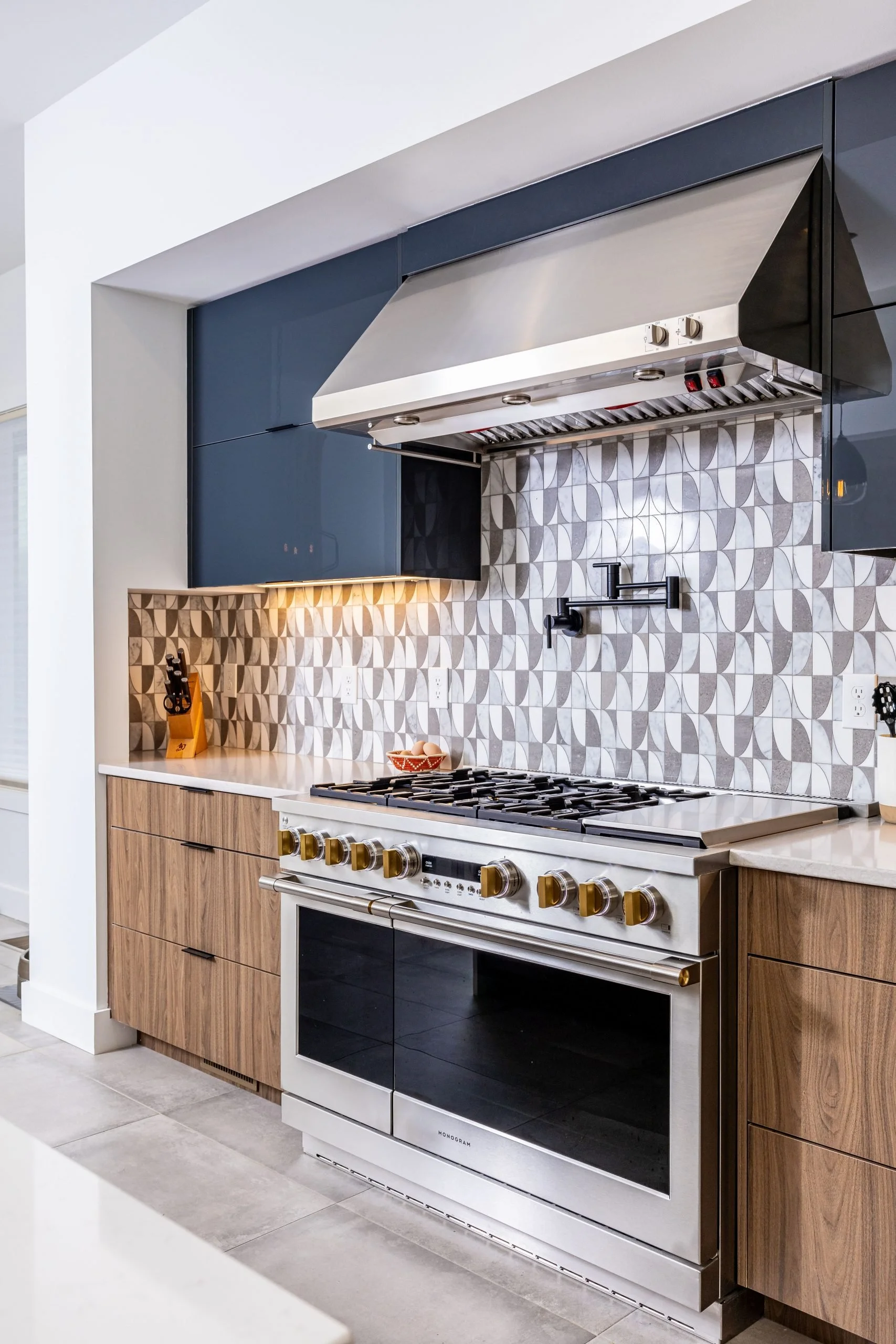 Mid-century modern kitchen design with custom flat-panel wood cabinets, quartz waterfall island, geometric tile backsplash, black pendant lights, and open-concept layout. A warm, modern kitchen with timeless mid-century influences.