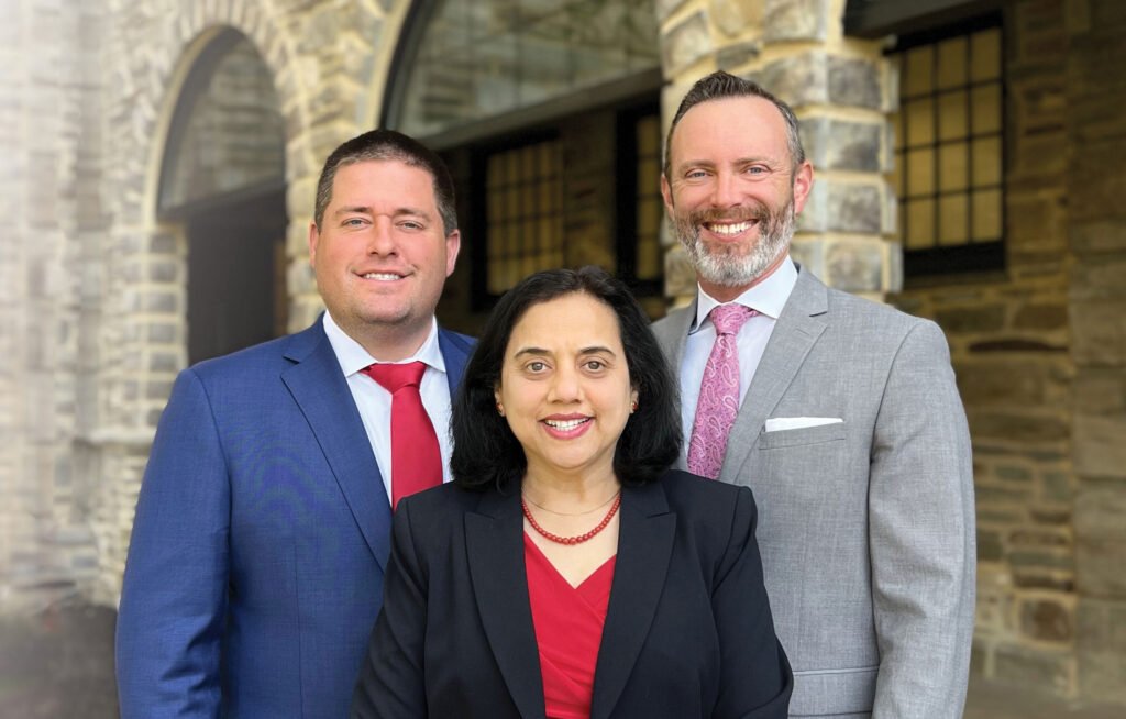 Three professionally dressed individuals, two men and one woman, standing outside in front of a stone building, smiling at the camera.