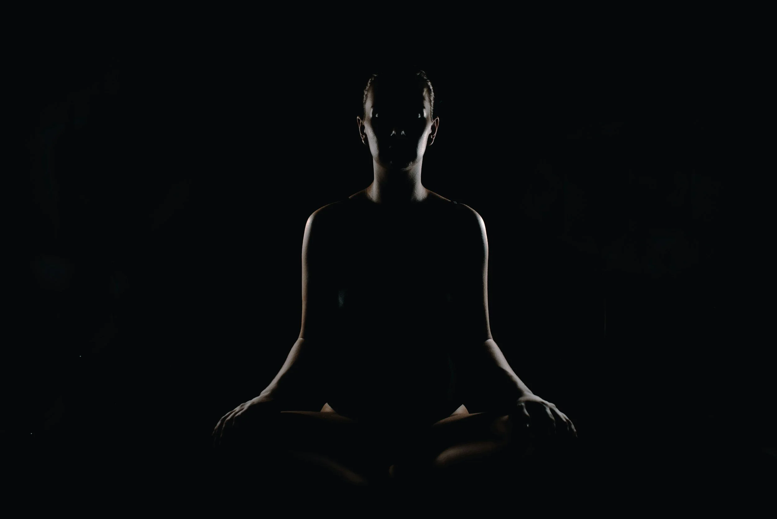 A person sitting in a meditative pose with silhouette against a dark background.