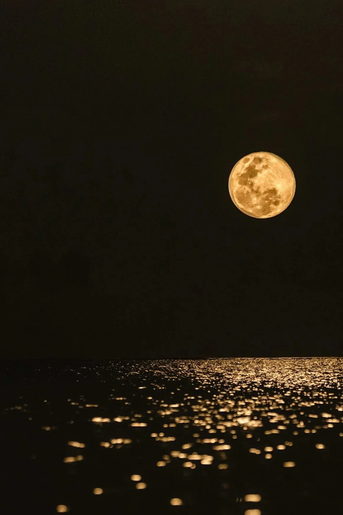 A bright full moon over a dark ocean with reflections on the water surface at night.