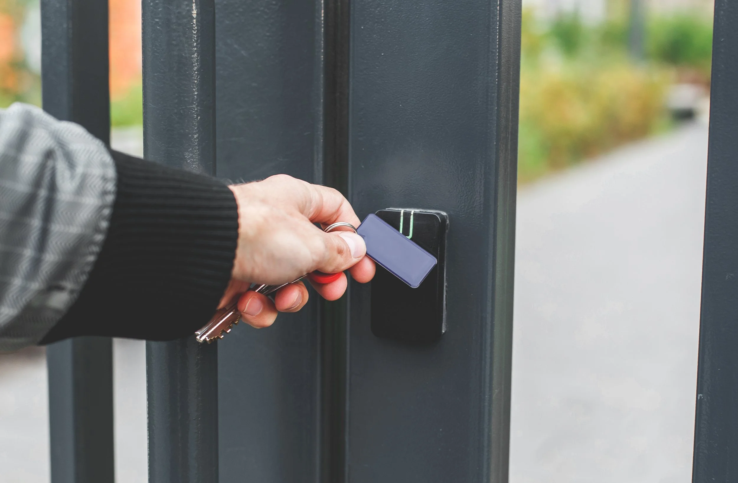 Person holding a keycard near an electronic access control keypad on a gate.