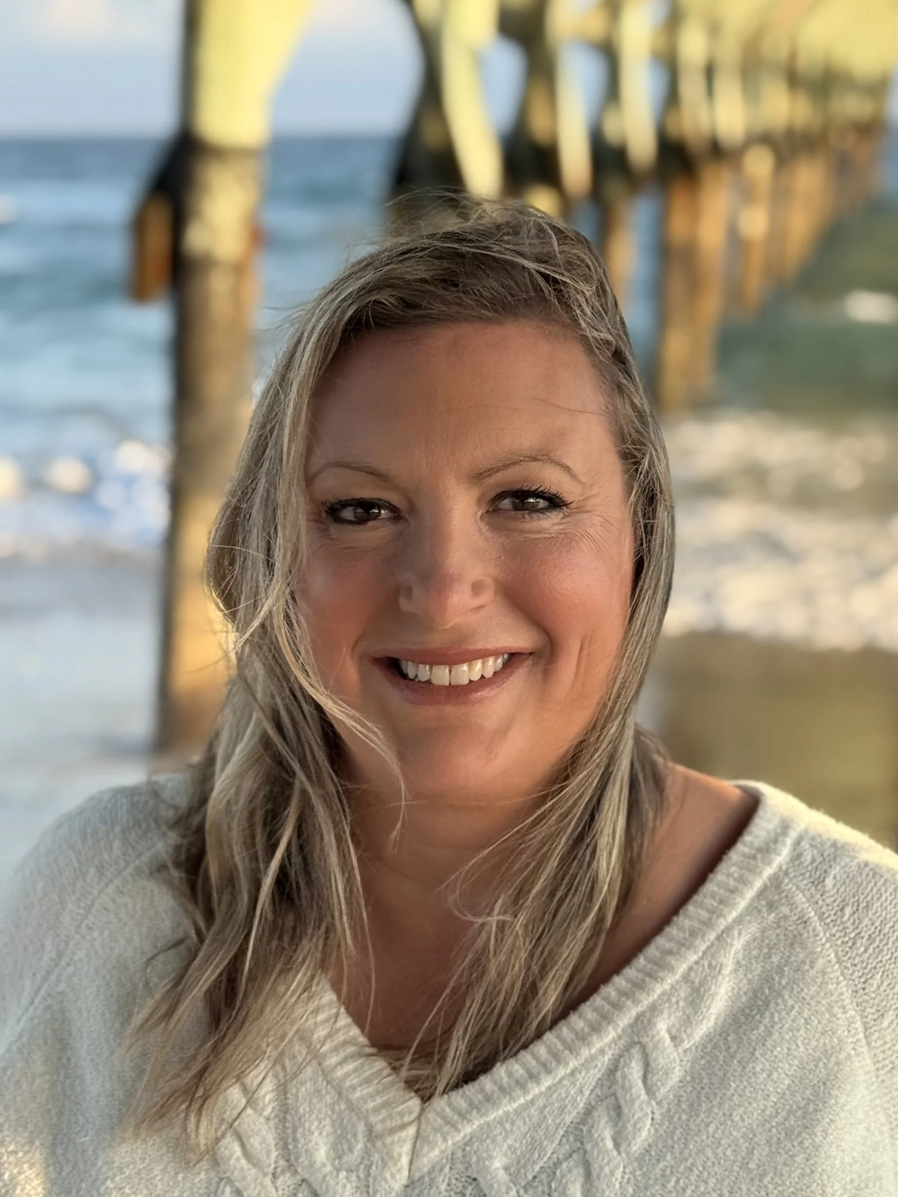 A female therapist smiling at the beach near a pier, the owner of Wilmington Couples Counseling.