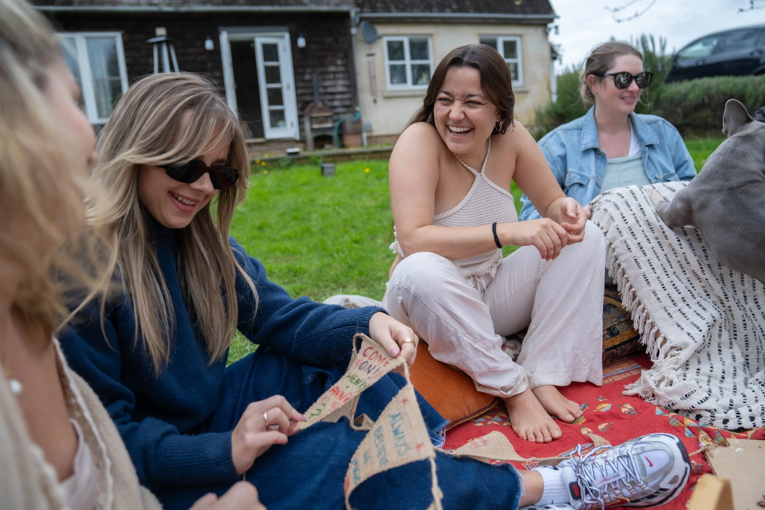Group of women sitting on a blanket and having fun outdoors in a backyard.