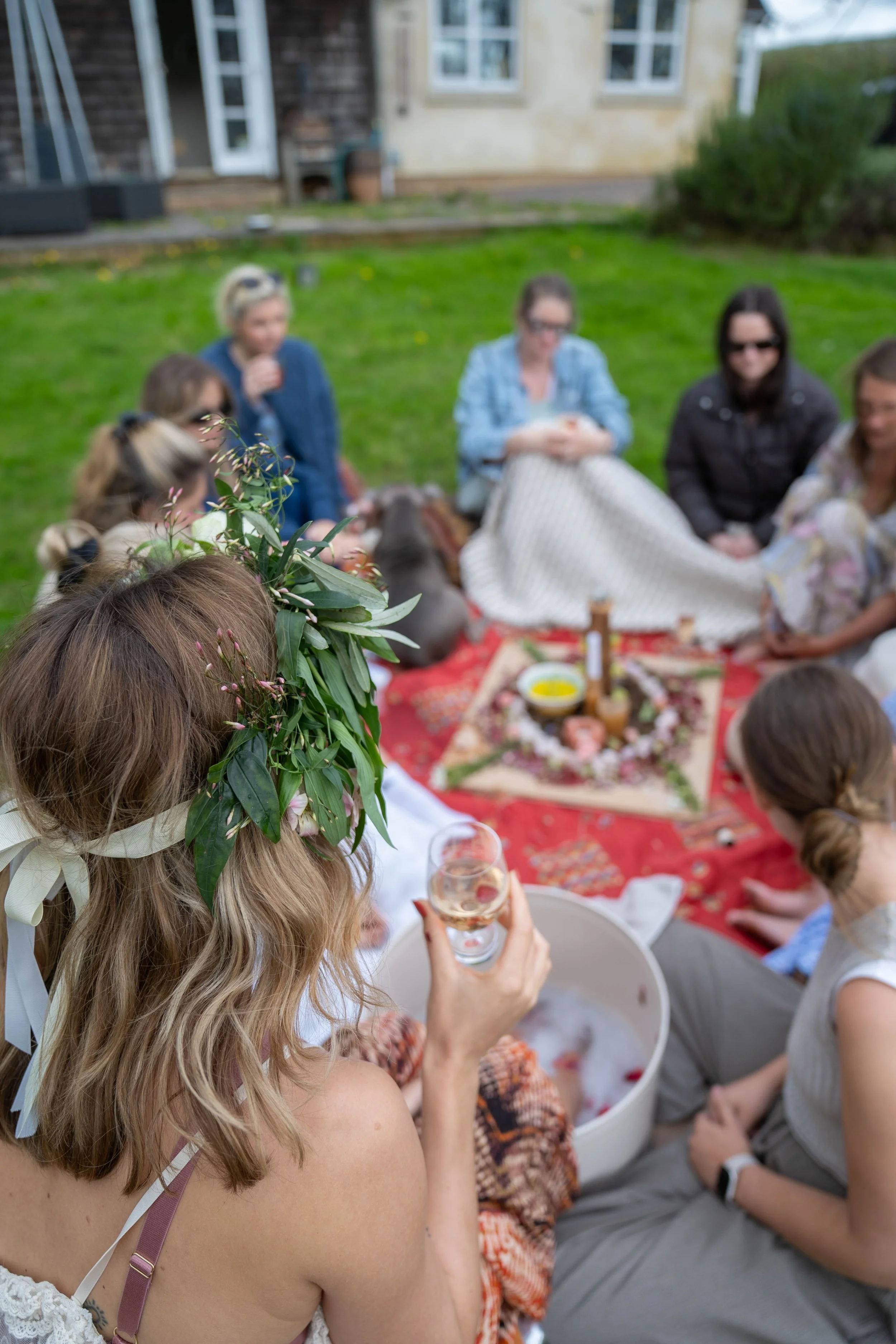 Group of women having a picnic outdoors on grass with a picnic spread and decorated table, celebrating in a garden area.