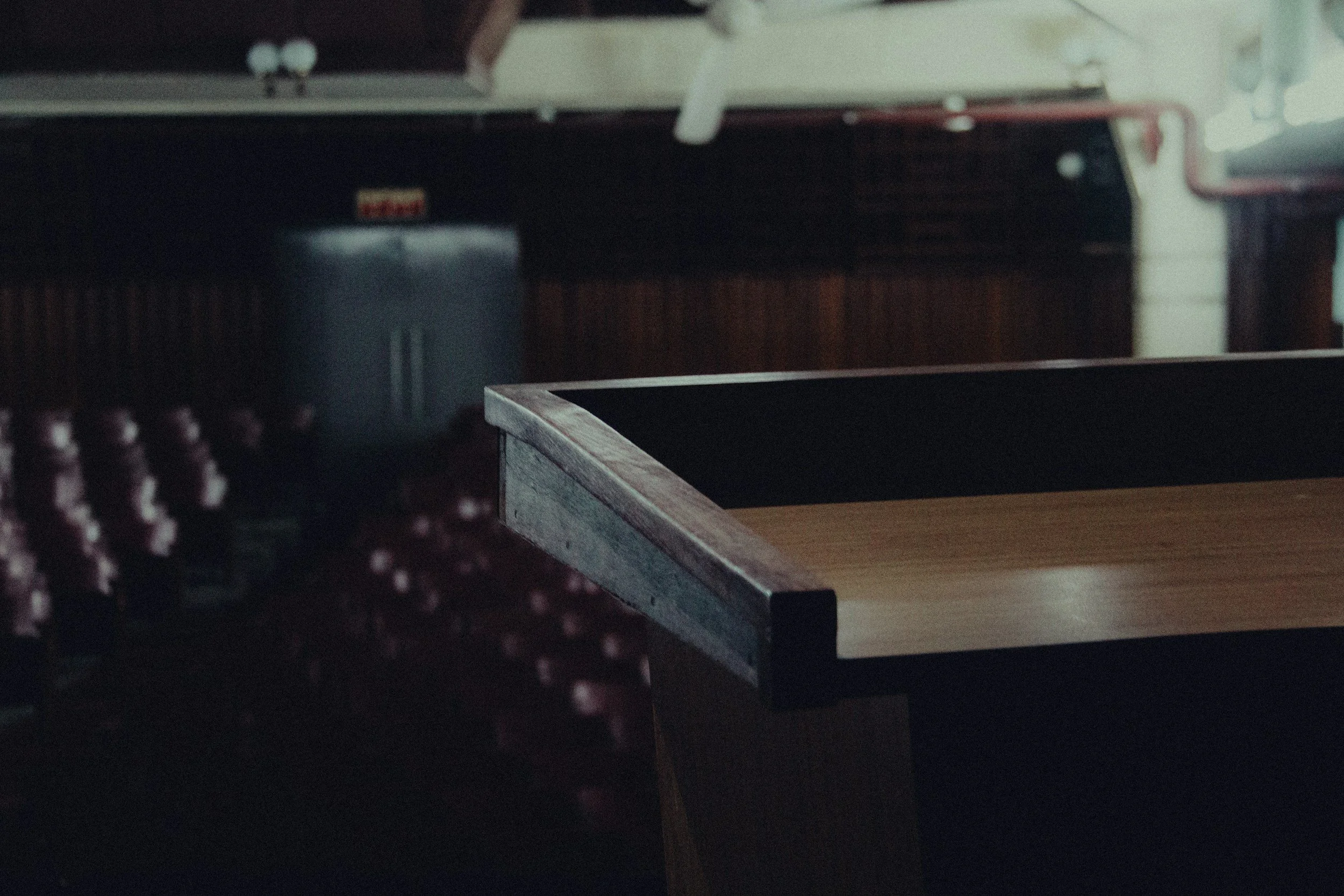 Close-up of a ping pong table in a dimly lit room, with empty red seats in the background.
