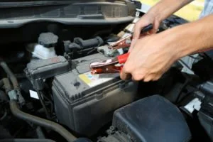 Person using pliers on car battery terminals under the hood.
