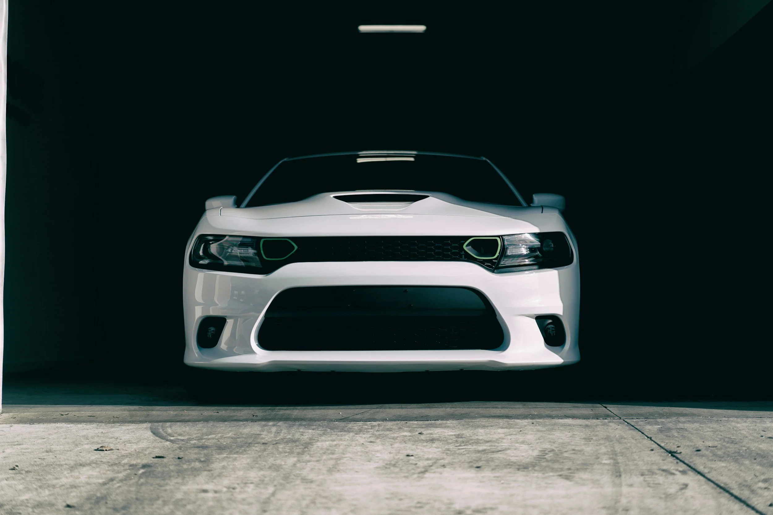 Front view of a white sports car parked inside a dark garage, with concrete floor.