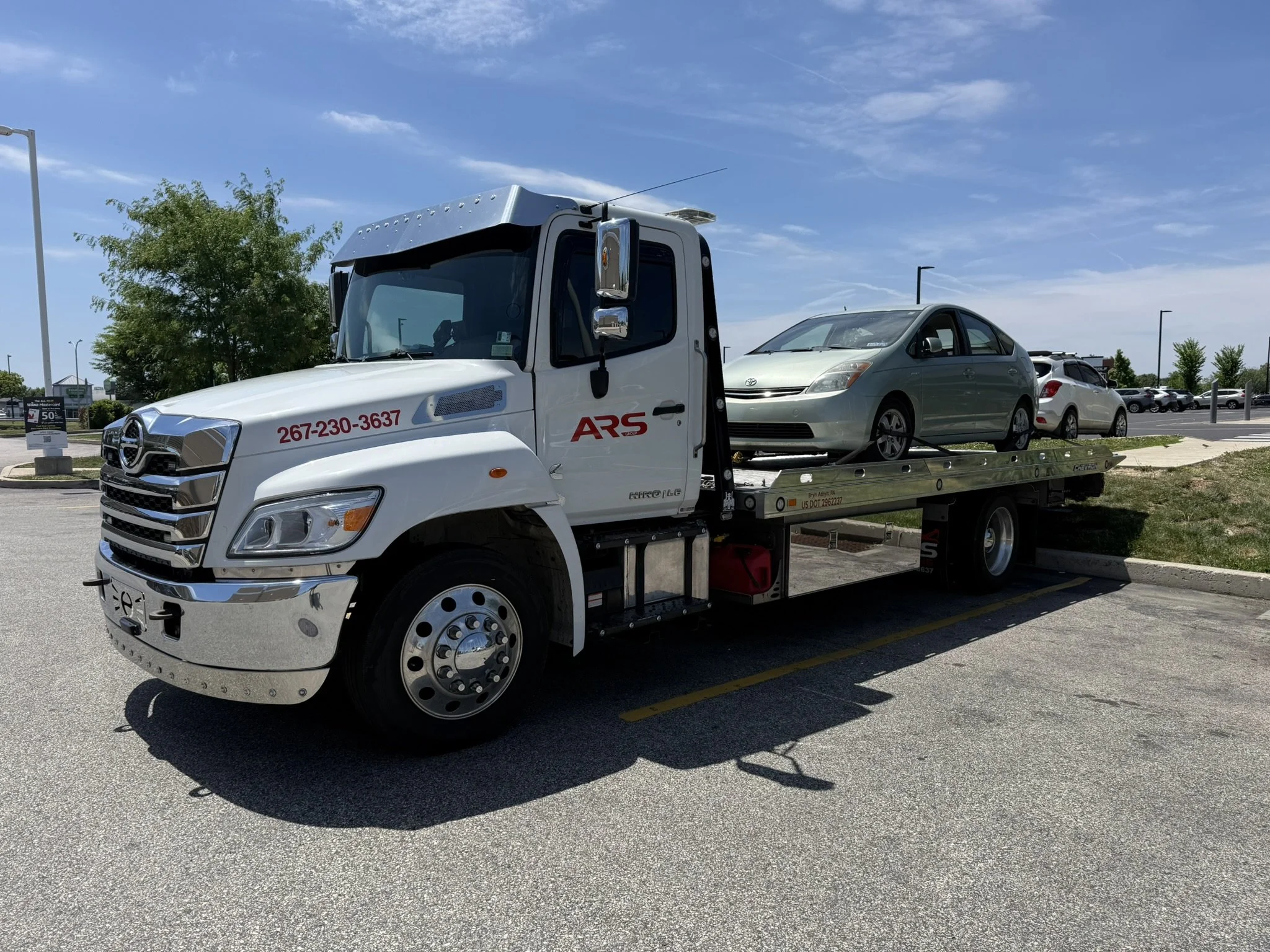 Flatbed tow truck providing vehicle transport and towing services for a silver sedan.