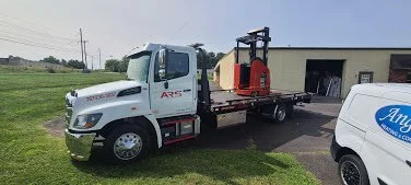 A white flatbed truck with a red crane is parked on a grassy area next to a building. There is a white van with an 'Angels' logo partially visible on the right.