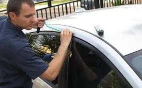 A man applying a strip of tape or film on the roof of a white car.