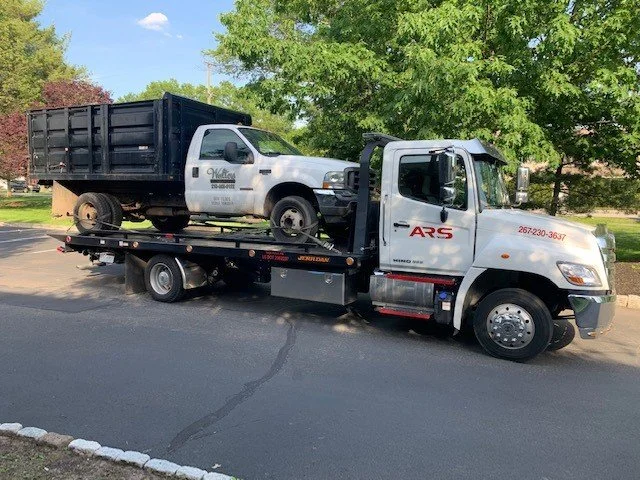 Tow truck carrying a black and white pickup truck with a flatbed.