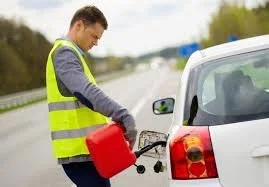 A man in a yellow safety vest refueling a car on the side of the road.